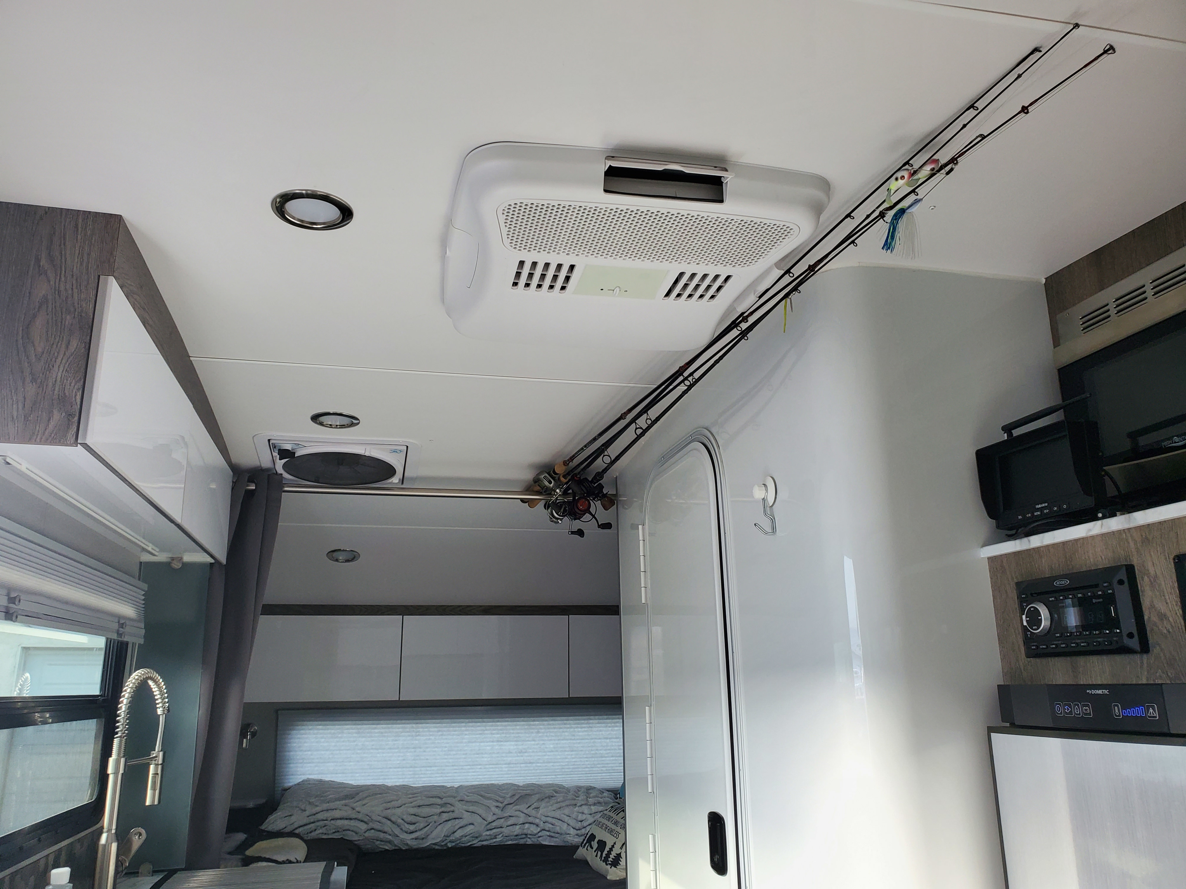 Inside an RV rental, showing clever overhead fishing rod storage. Features a bed, kitchen sink, and entertainment system.. InTech RV Sol Horizon 2020