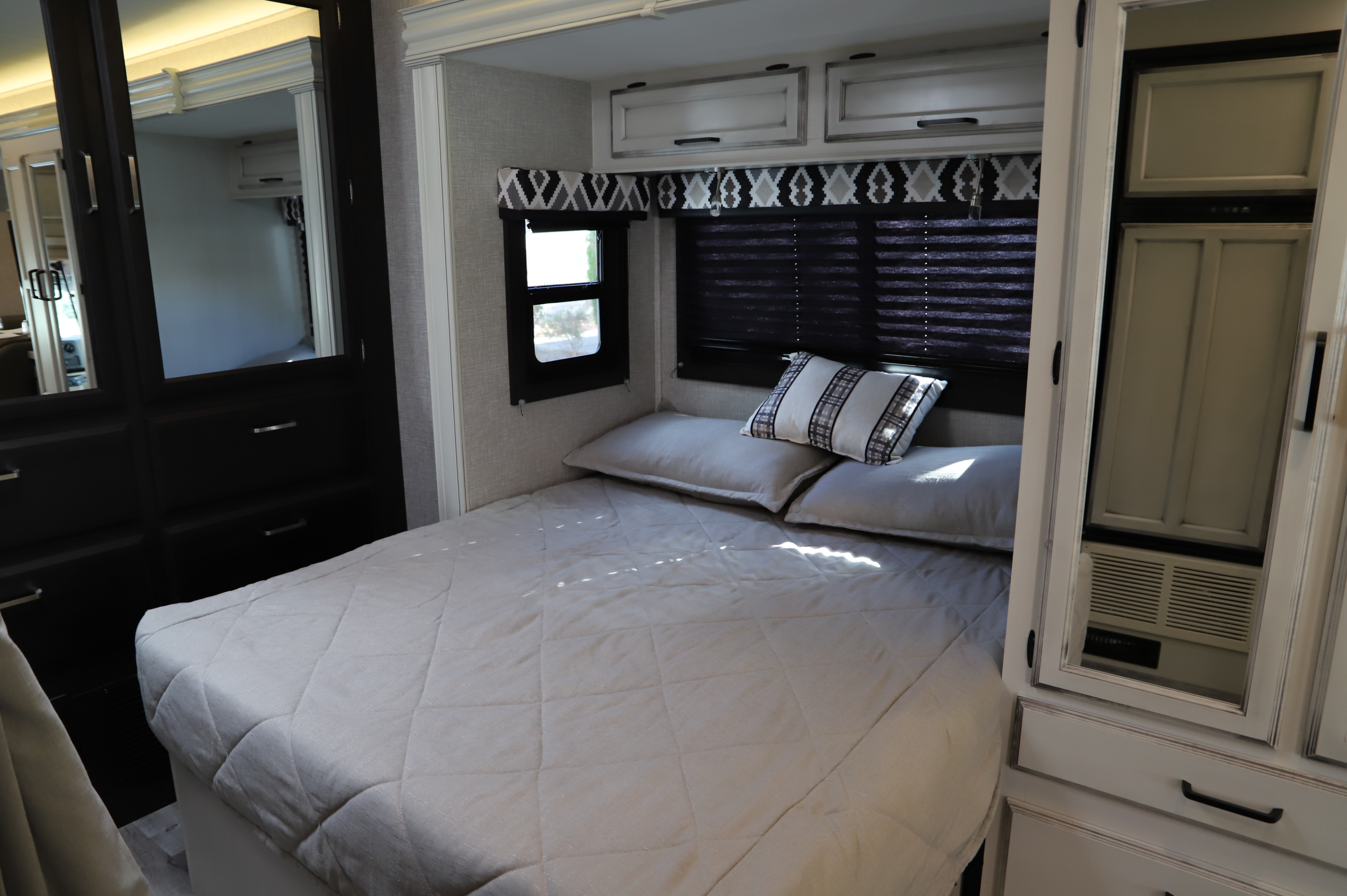 Modern RV rental bedroom interior with a comfy bed, striped pillow, white cabinets, and mirrored wardrobe on the left.. Entegra 24B 2022