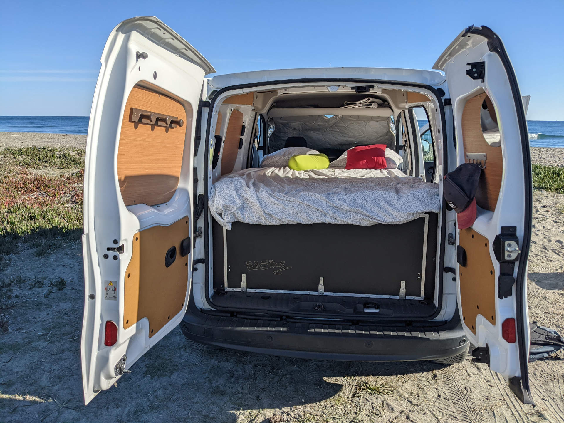 RV rental: Rear view of a camper van with a comfortable bed, EASibox storage, on a sandy beach. Perfect for travel!. Renault Kangoo 2015