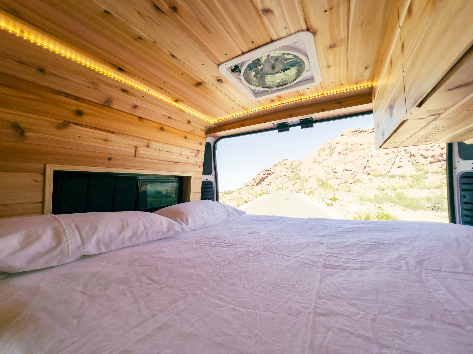 RV rental: Comfy bed in wood-paneled van interior, opening to a desert road and mountains. Ideal for road trips.. Dodge Other 2021