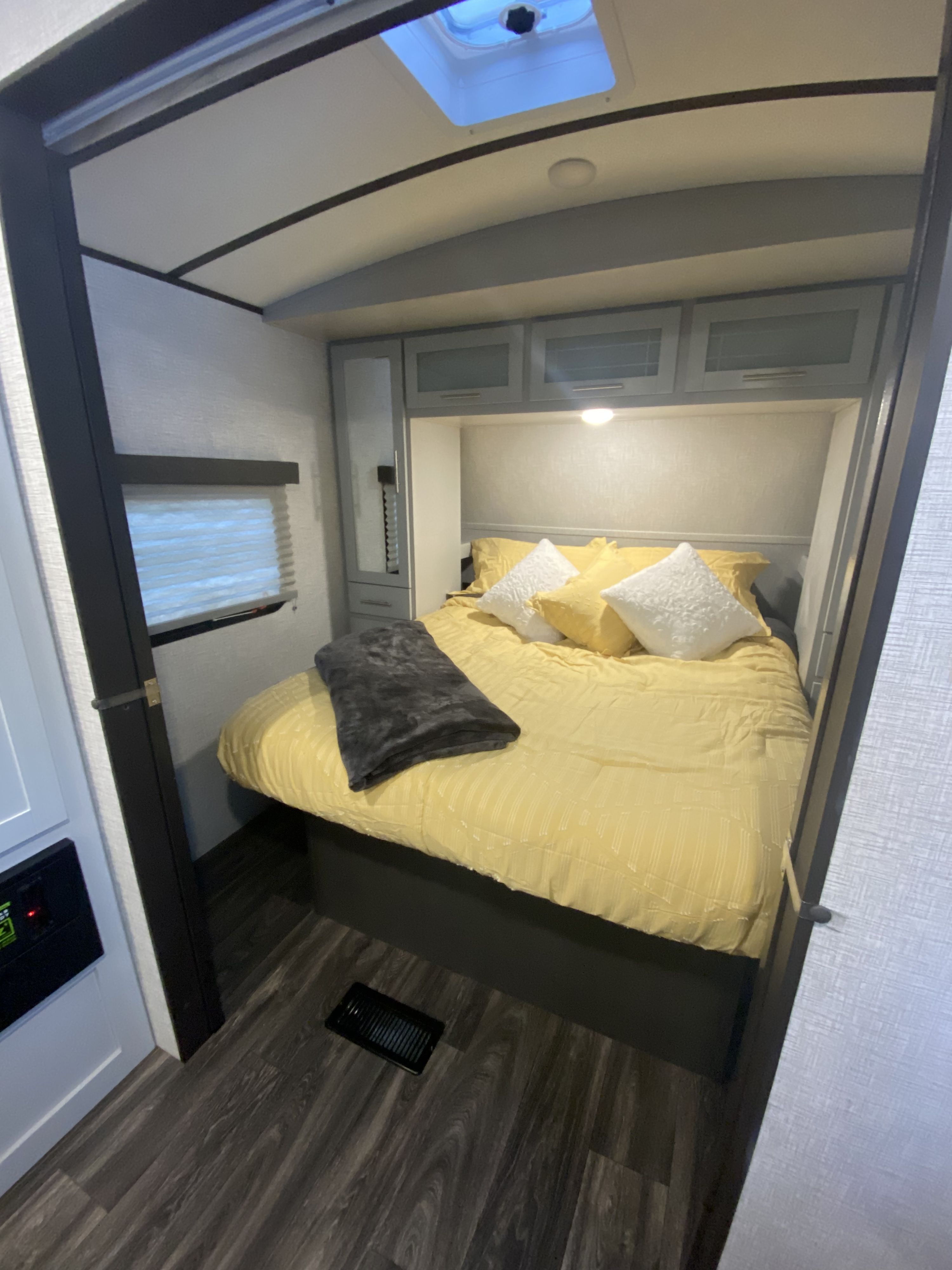 Cozy RV rental bedroom with bright yellow bedding, white pillows, gray cabinets, and dark wood-look floor.. Keystone RV Bullet Ultra Lite 2021