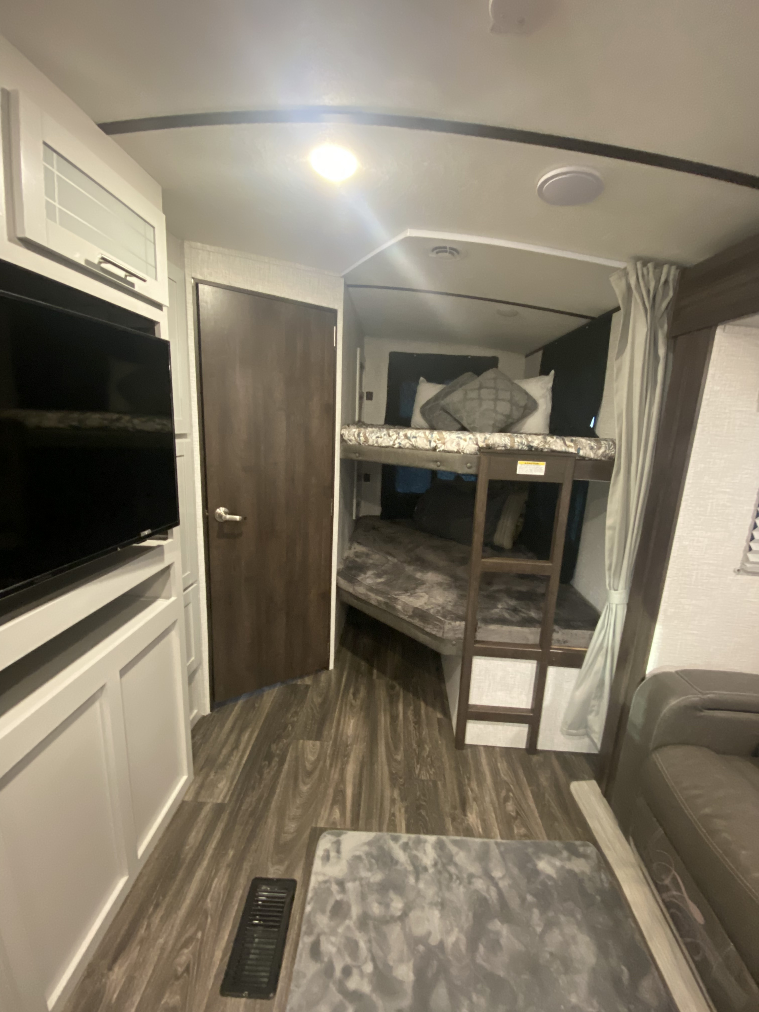 Modern RV rental living area featuring a mounted TV, a door, and cozy bunk beds. Perfect for family adventures.. Keystone RV Bullet Ultra Lite 2021
