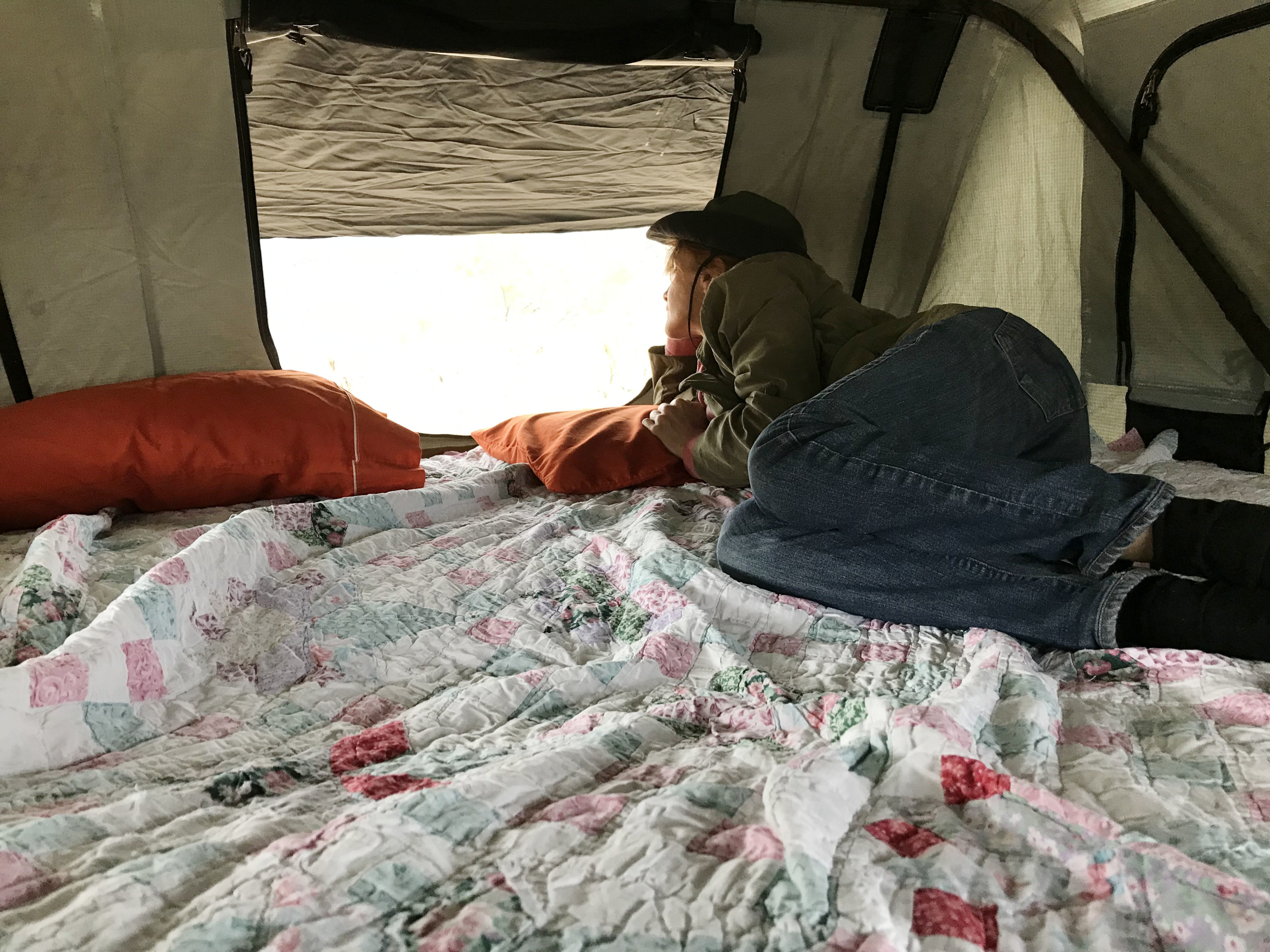 Enjoying the view from inside an RV rental! A person lies on a comfy quilt with pillows, looking out a bright window.. Jeep Cherokee 2001