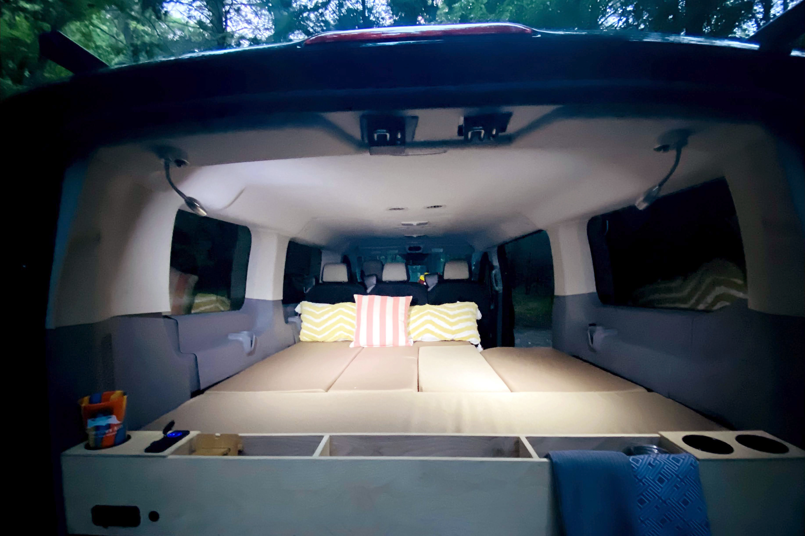 Interior of a customized van conversion featuring a cozy portable bed, pillows, and storage. Perfect for camping or an RV rental adventure.. Ford Transit 2015