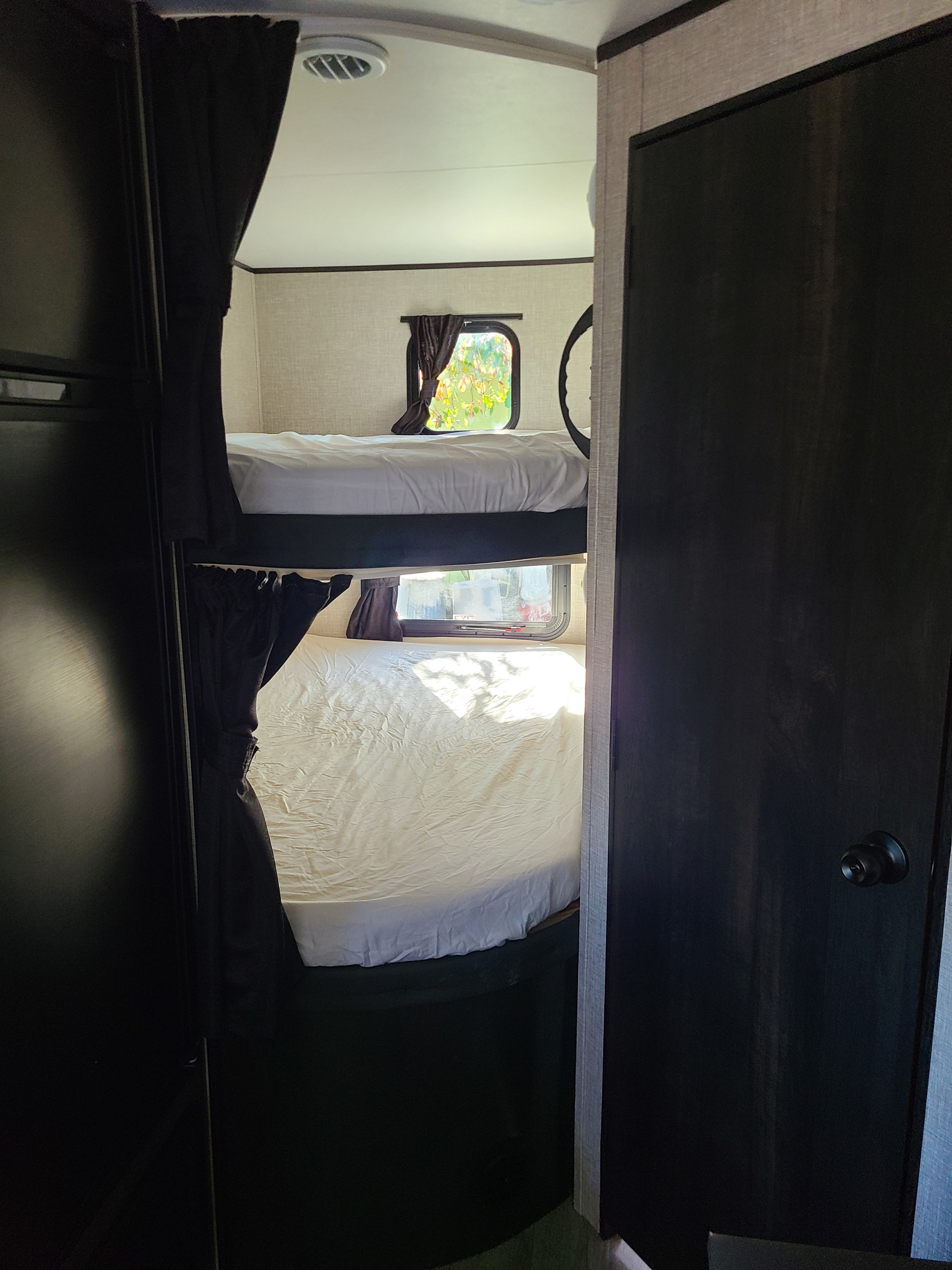 Cozy bunk beds in an RV rental, featuring white bedding, dark curtains, and natural light from small windows.. Jayco 224BHW RME BAJA 2022