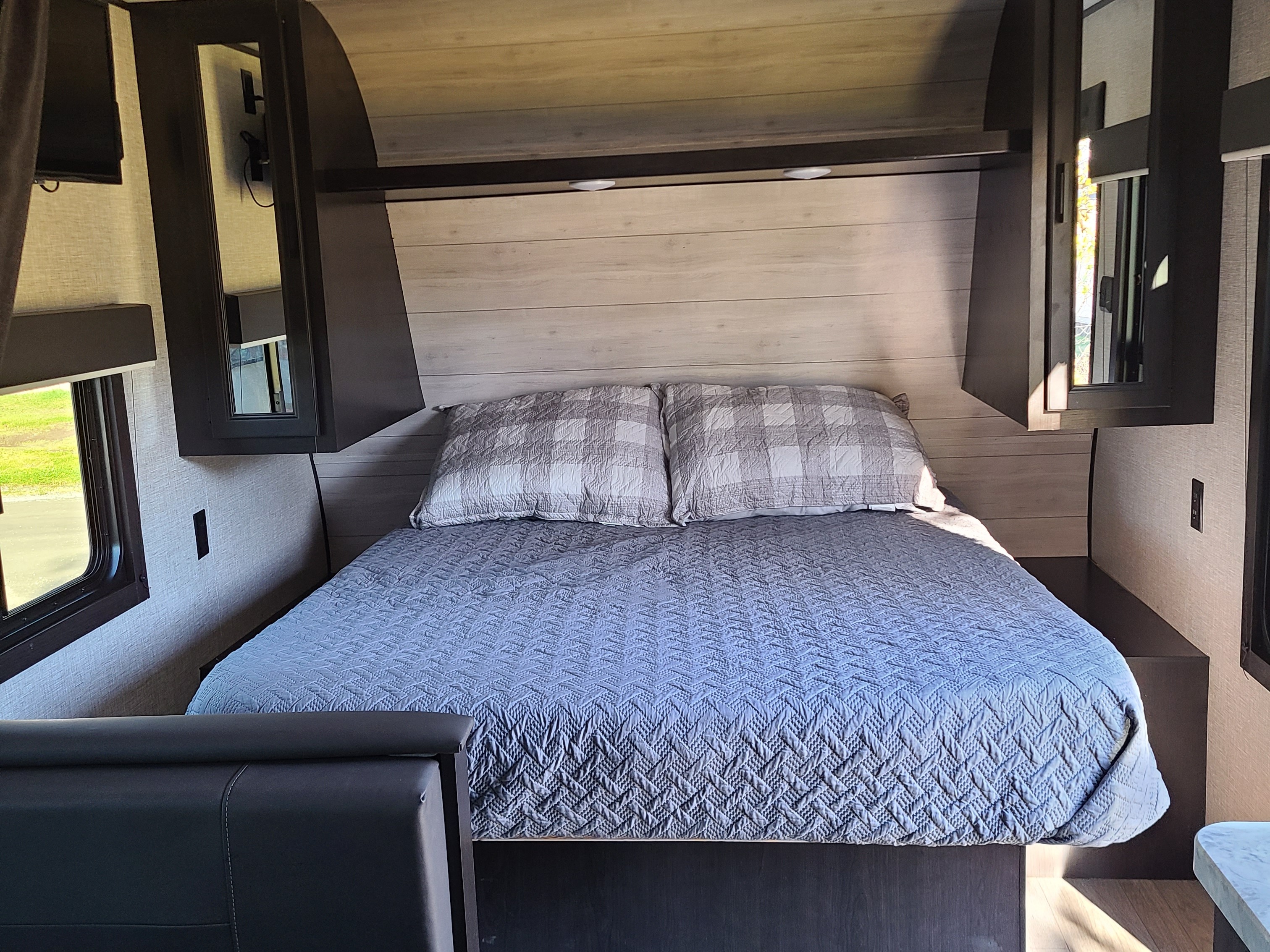 Cozy RV rental bedroom interior featuring a bed with a blue quilt, pillows, overhead storage, and a window.. Jayco 224BHW RME BAJA 2022