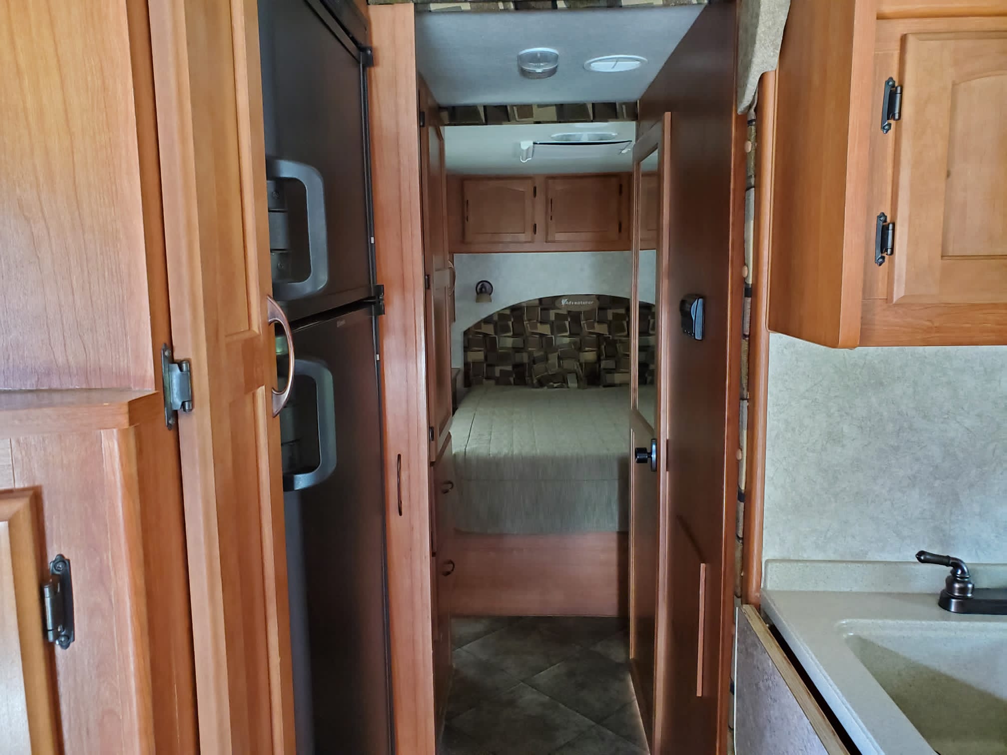 RV rental interior shows a compact kitchen with sink, refrigerator, and a hallway leading to a cozy bedroom.. Adventurer Ford Adventurer RV 2014