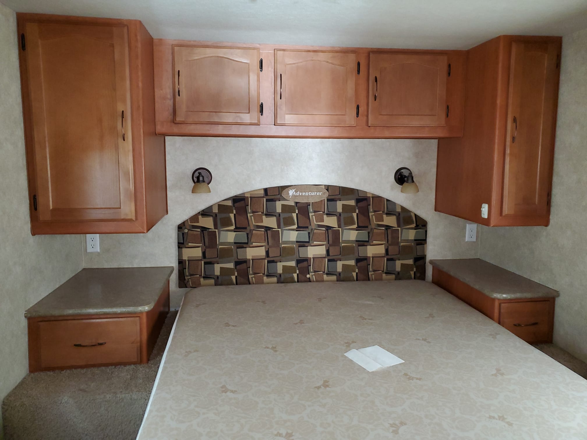 RV rental bedroom featuring a bed, patterned headboard, overhead wooden cabinets, and convenient side storage. Ready for your trip.. Adventurer Ford Adventurer RV 2014
