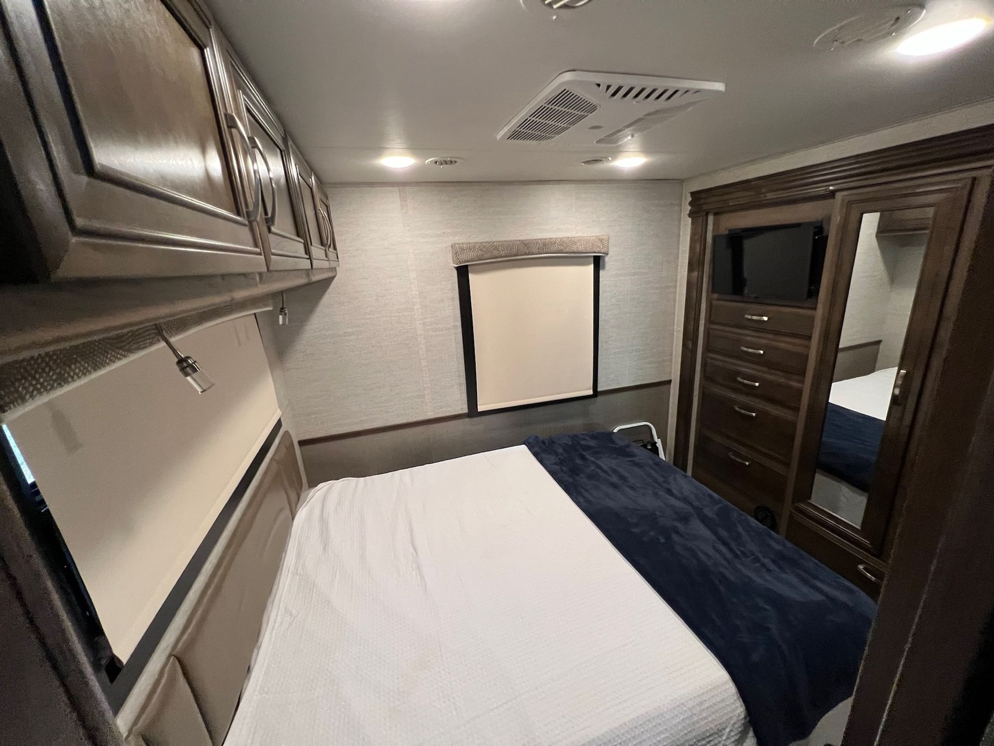 Cozy RV rental bedroom features a neatly made bed, overhead cabinets, TV unit, and mirrored closet.. Entegra Coach Vision 2021