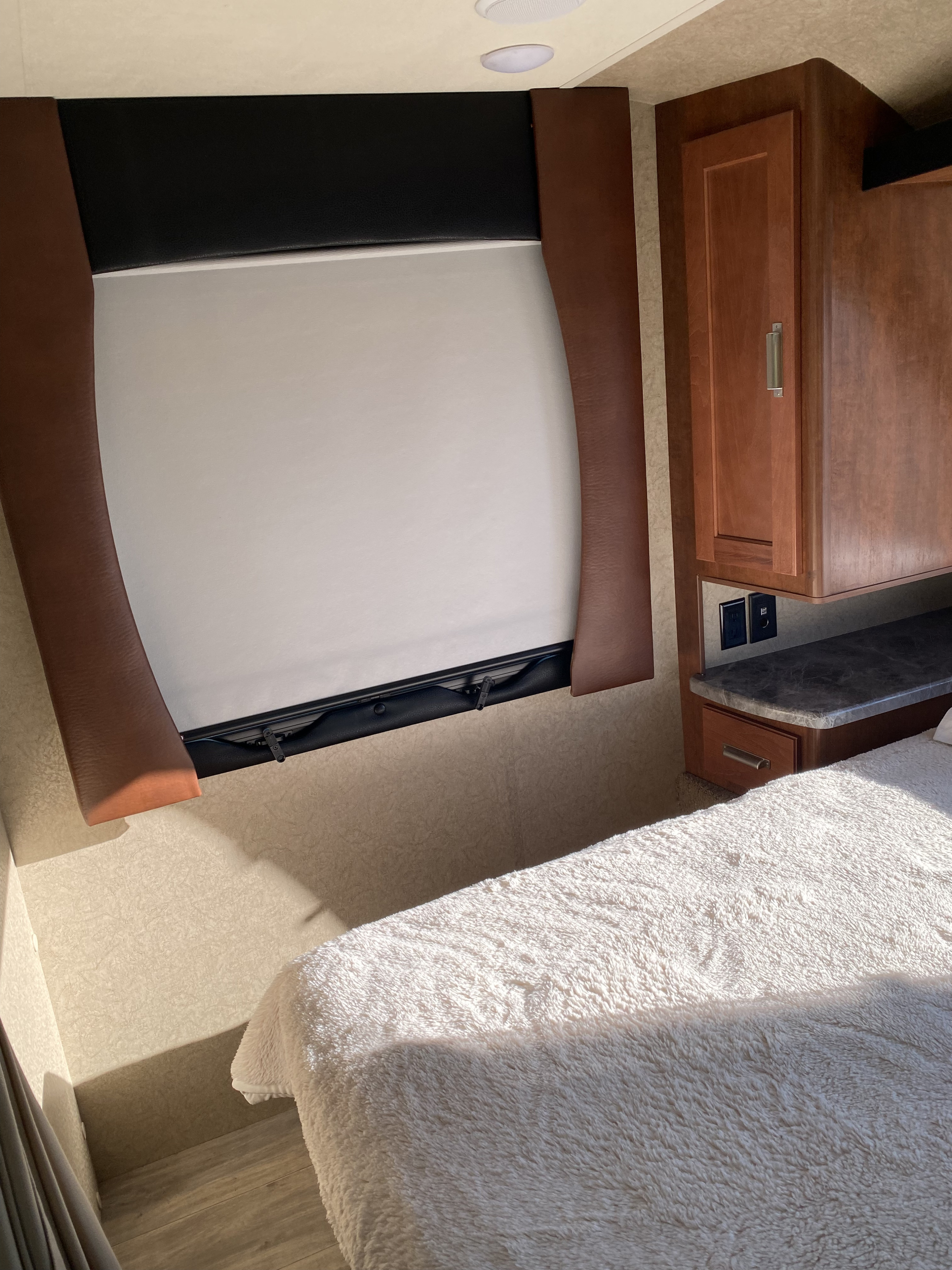 Cozy RV rental bedroom featuring a large window with a pull-down shade, plush bed, and convenient cabinet storage.. Lance Manufacturing 2375 2021