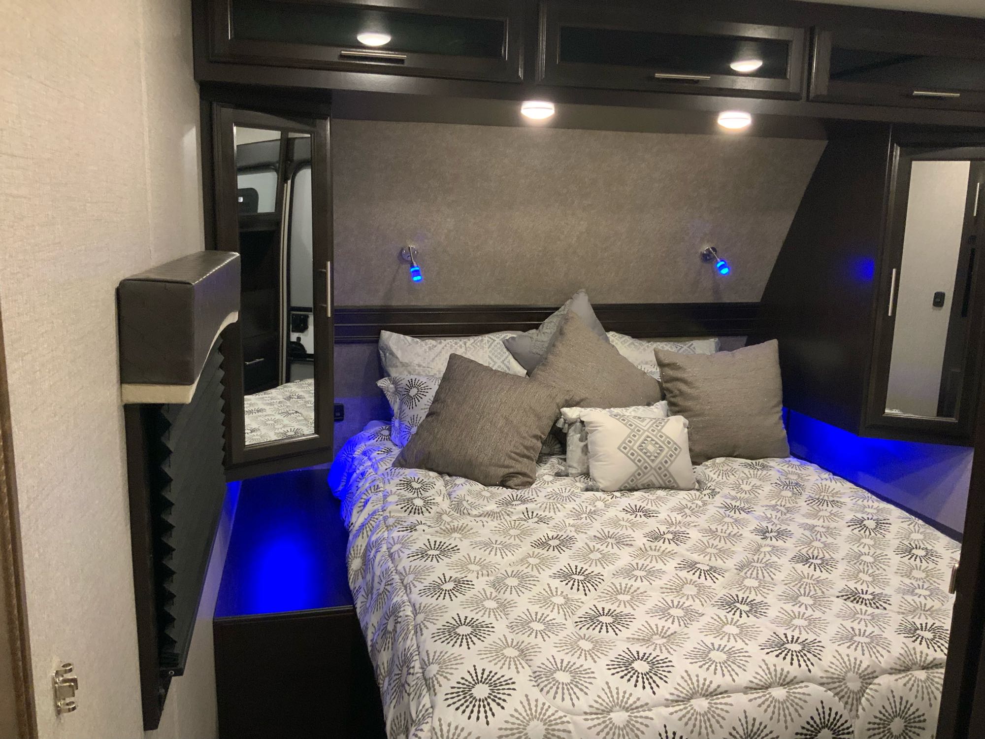Cozy RV rental bedroom featuring a patterned bed, dark wood, and serene blue accent lighting. Mirrors enhance the space.. Jayco Eagle HT 2019