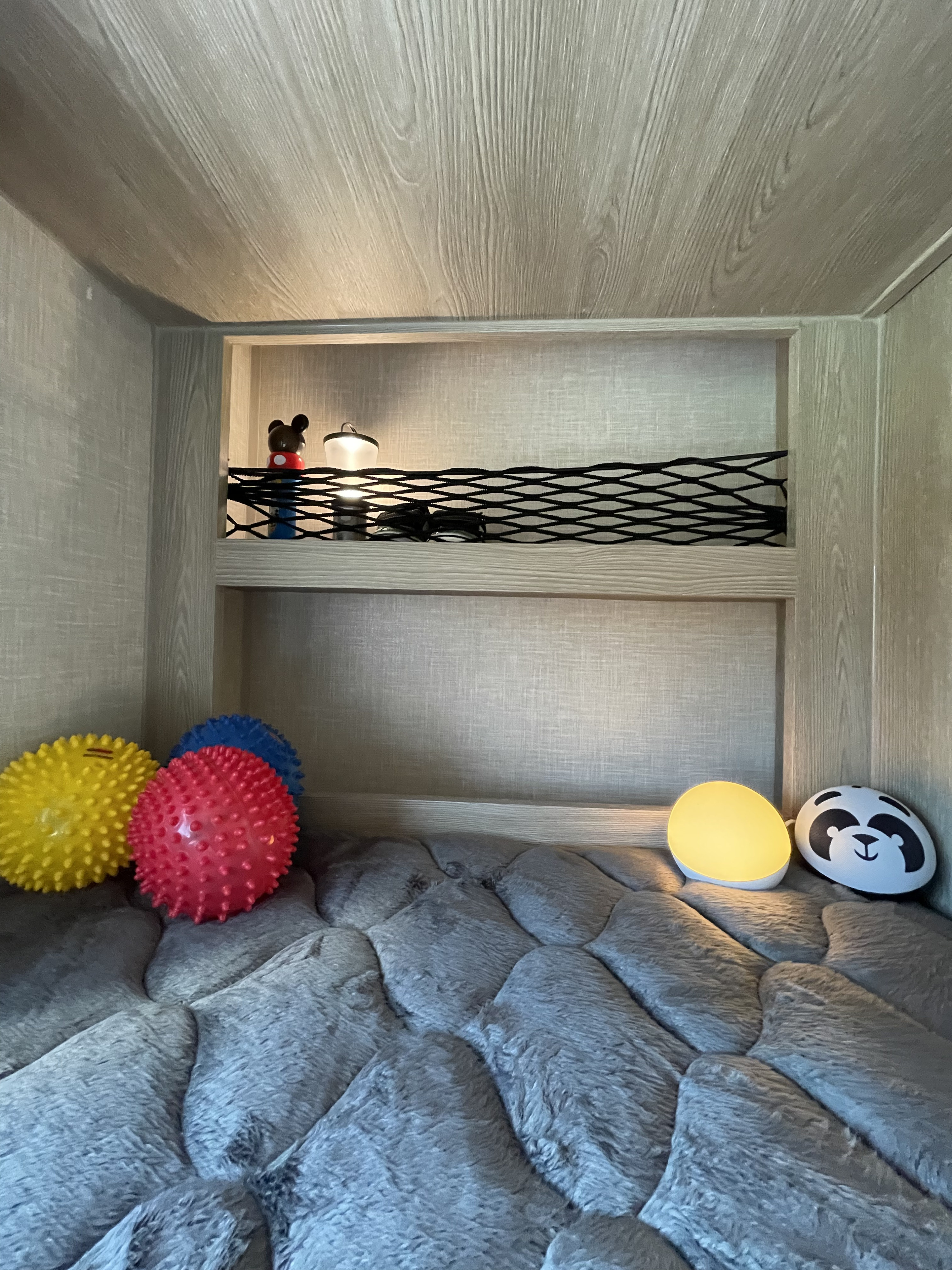 Inside a cozy RV rental: a bunk with sensory balls, two night lights, and shelf items like a Mickey figure.. Forest River Flagstaff E-Pro 2021