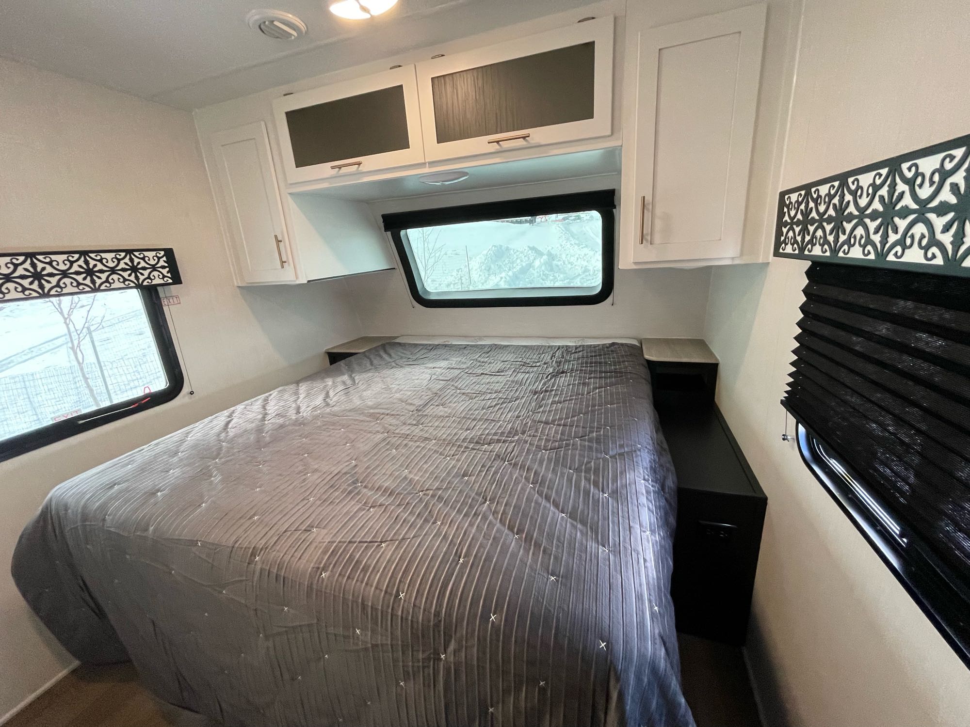 Clean RV rental bedroom with a gray bed, white cabinets, and winter window views, ideal for cozy travel.. Forest River 303MBX 2022