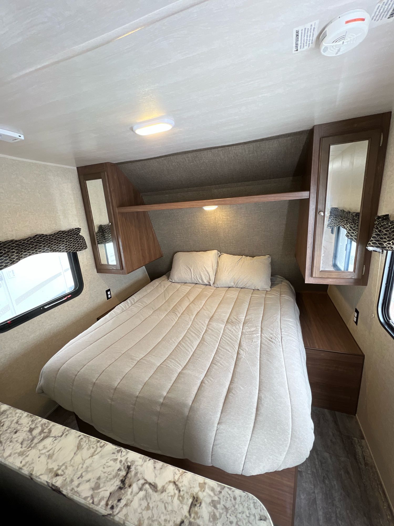 This RV rental features a cozy bedroom with a comfortable bed, mirrored storage cabinets, and natural light from side windows.. Heartland RVs Trail Runner SLE 2017