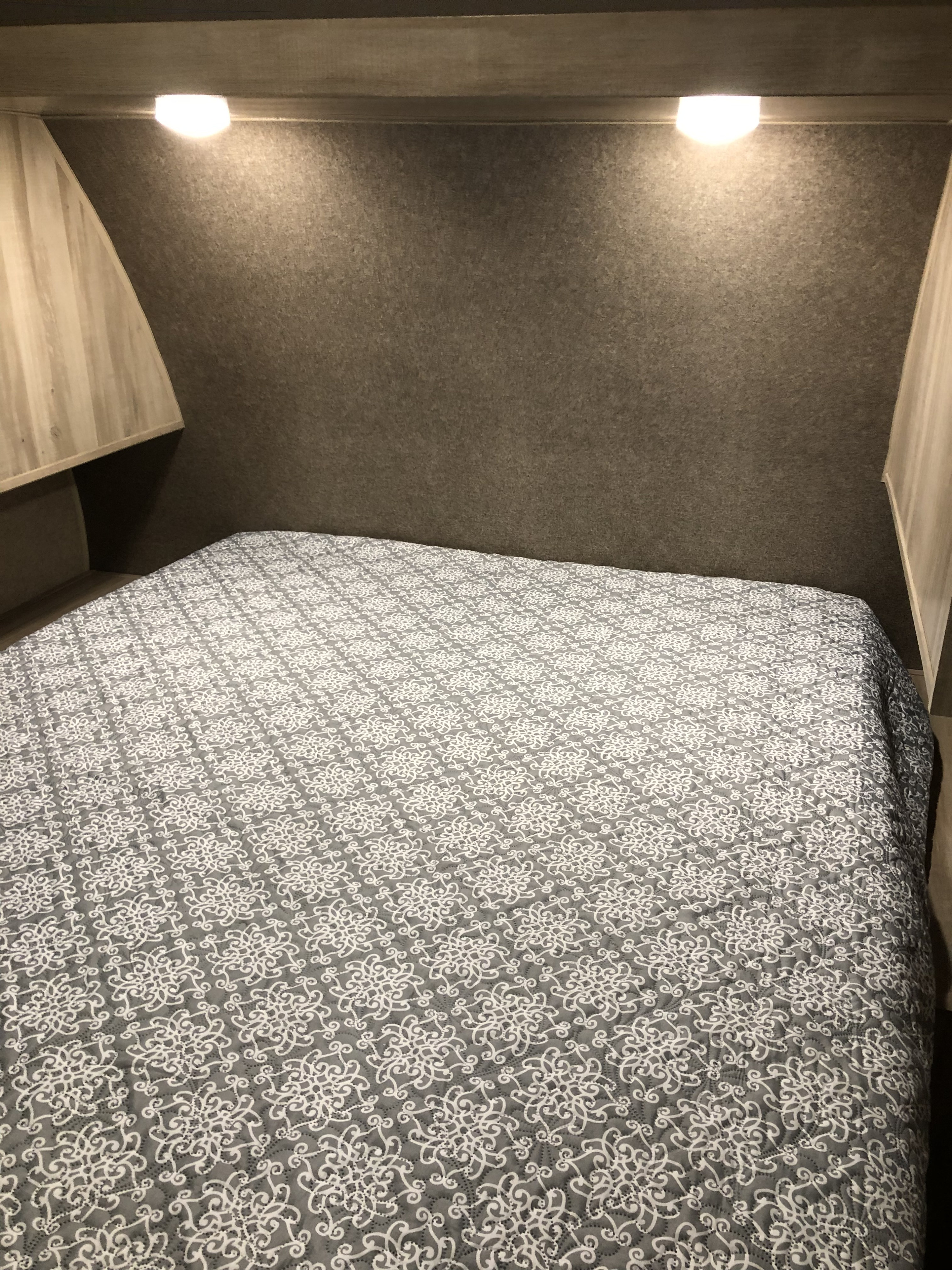 An RV rental bedroom showcasing a comfy bed with a gray patterned quilt, overhead reading lights, and convenient storage.. Coachmen Catalina SBX 221TBS 2019