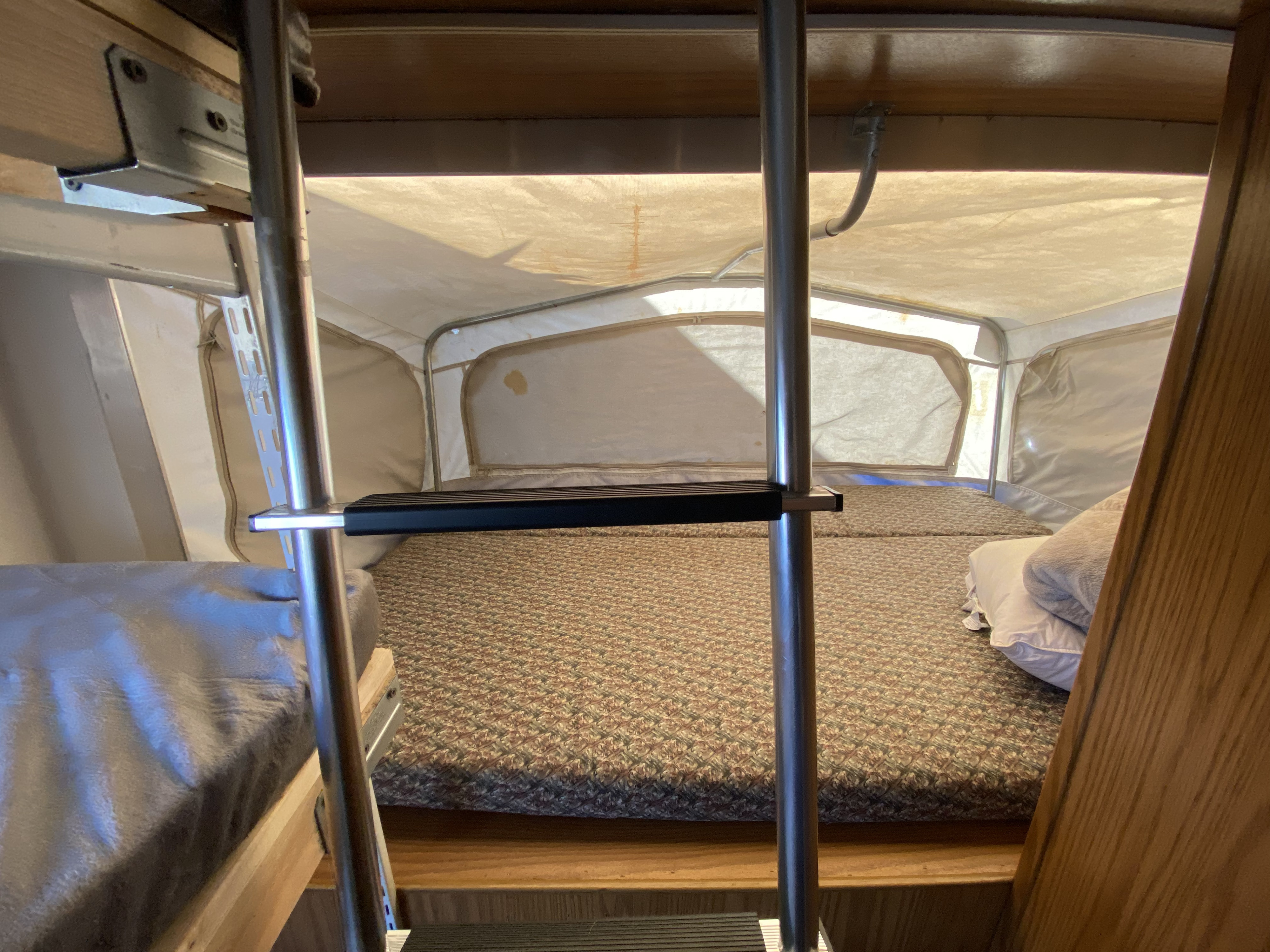 Inside an RV rental pop-up camper: a bed with patterned mattress, canvas walls, and a ladder to an upper bunk.. Starcraft Travel Star 2002