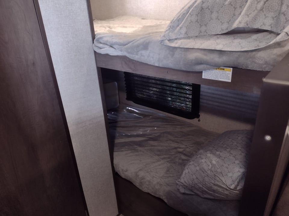Interior view of an RV rental: two compact, comfortable bunk beds with bedding, ready for your next travel adventure.. Coleman Lantern 17B 2022
