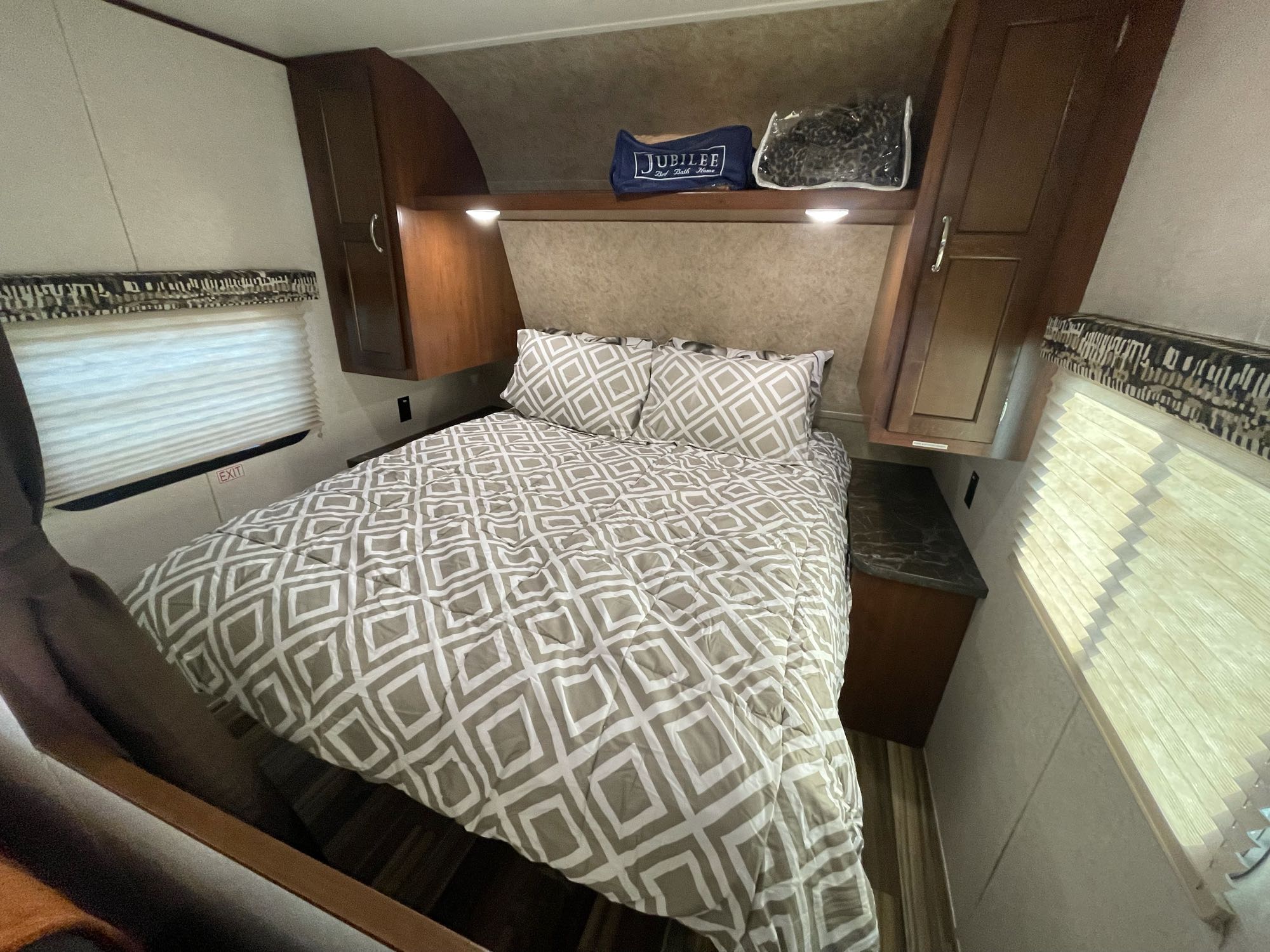 Inside a cozy RV rental bedroom: a bed with patterned bedding, built-in cabinets, and window blinds.. Jayco Jay Flight 2017