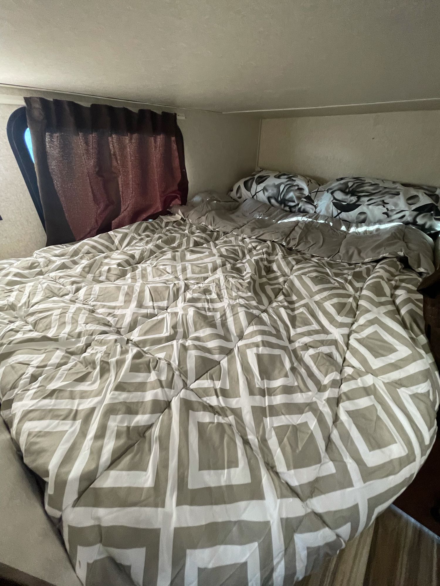 Comfortable sleeping area in an RV rental, featuring a bed with patterned comforter, pillows, & curtain.. Jayco Jay Flight 2017