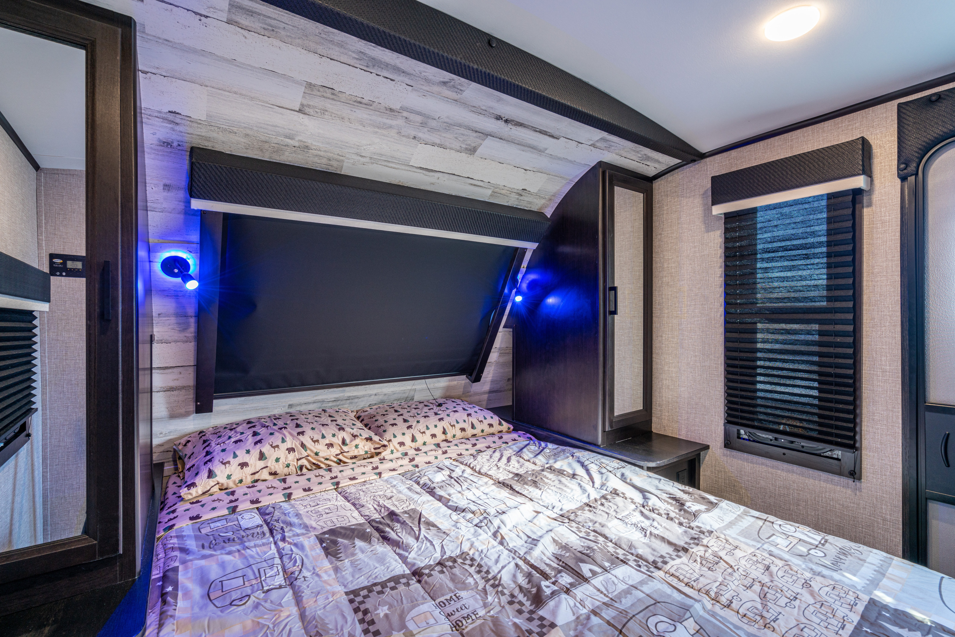Cozy RV rental bedroom featuring patterned bedding, blue accent lighting, and window blinds.. Jayco White Hawk 29BH 2022