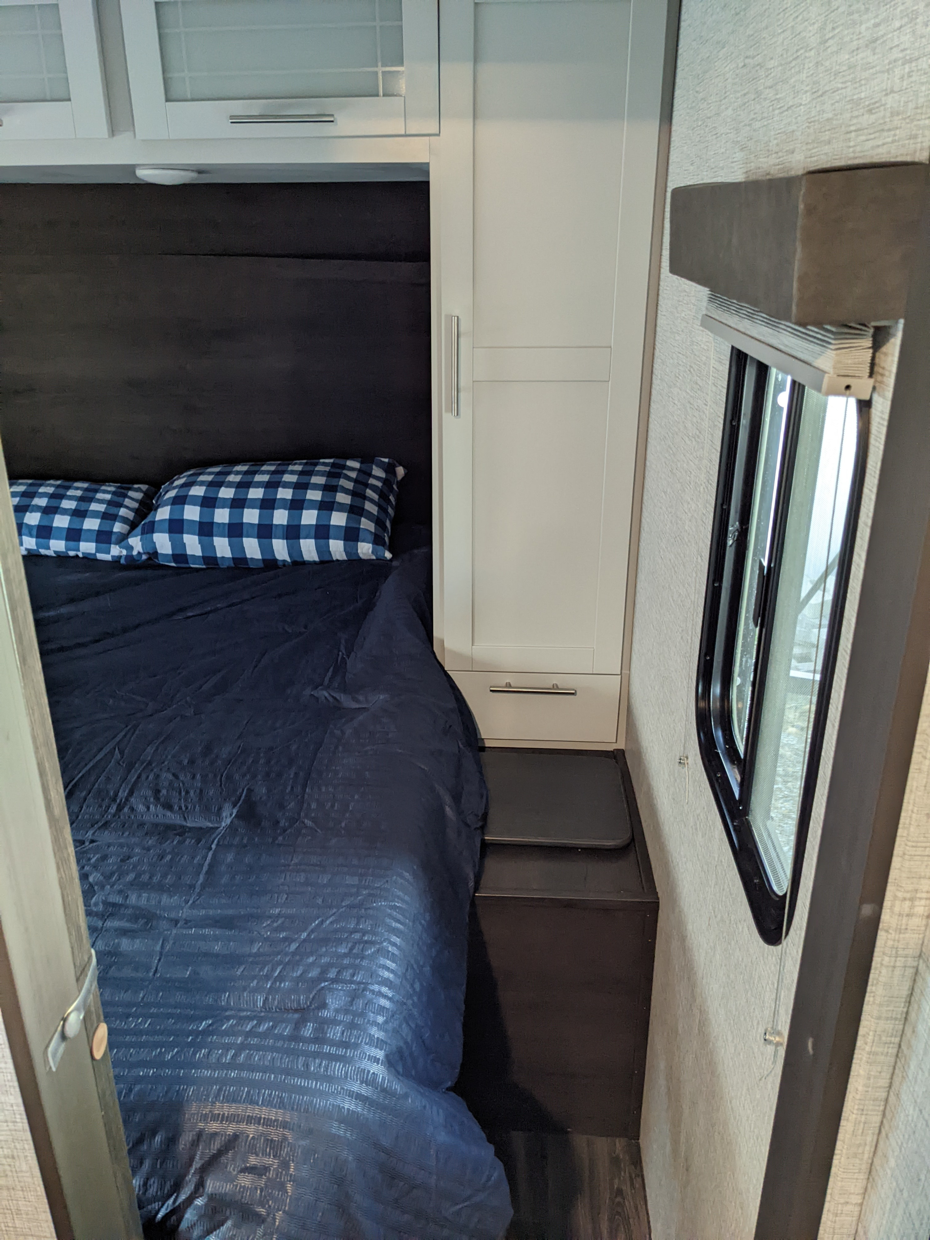 RV rental bedroom interior: Features a bed with blue bedding & checkered pillows, white cabinets, and a window.. Keystone RV Bullet Ultra Lite 2021