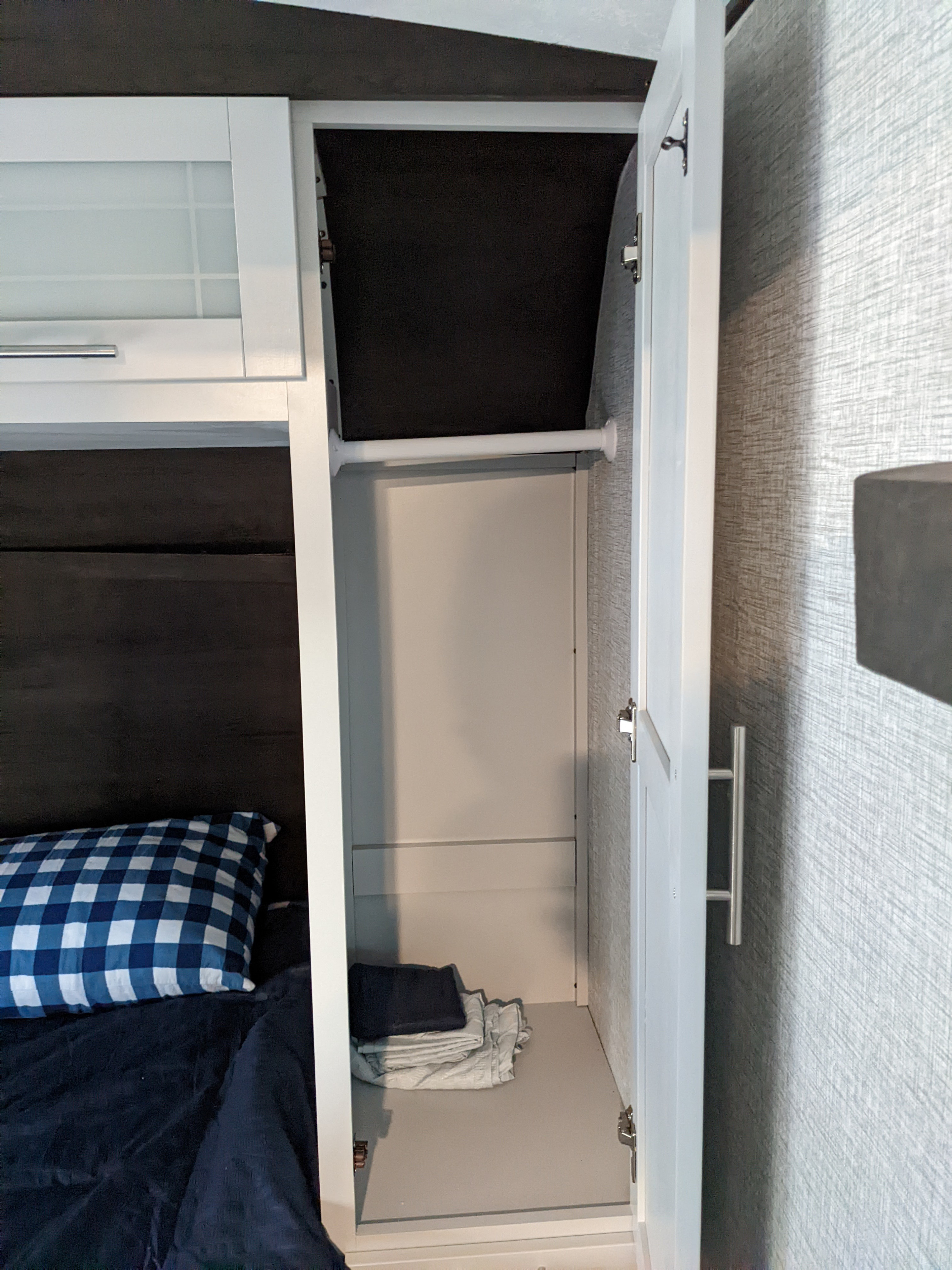 RV rental bedroom: a bed with a blue pillow, an overhead cabinet, and an open wardrobe for compact storage.. Keystone RV Bullet Ultra Lite 2021