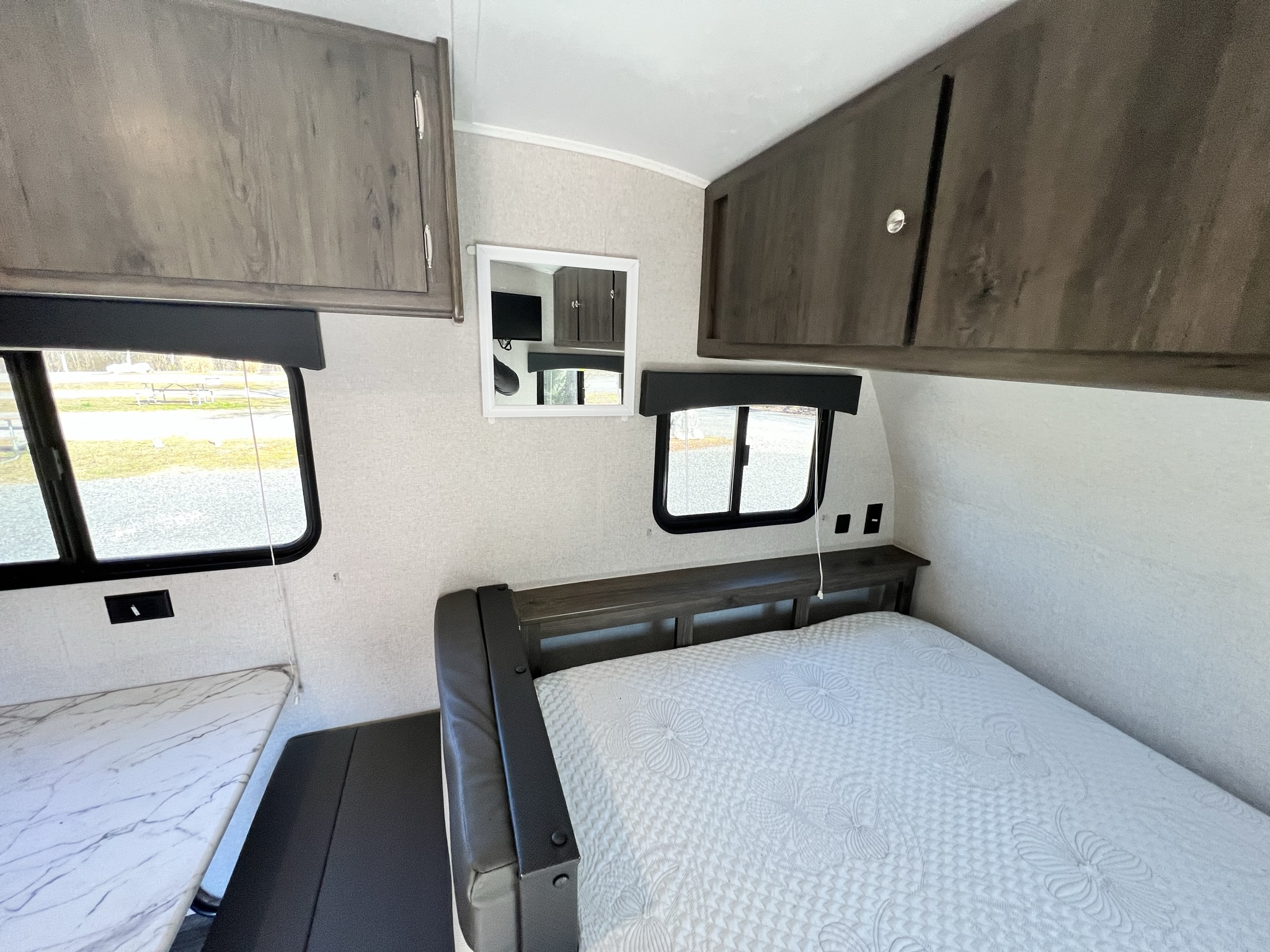 Interior of an RV rental: a compact bedroom with a white quilted bed, overhead cabinets, and a side dinette for comfortable travel.. Forest River 17BH 2021