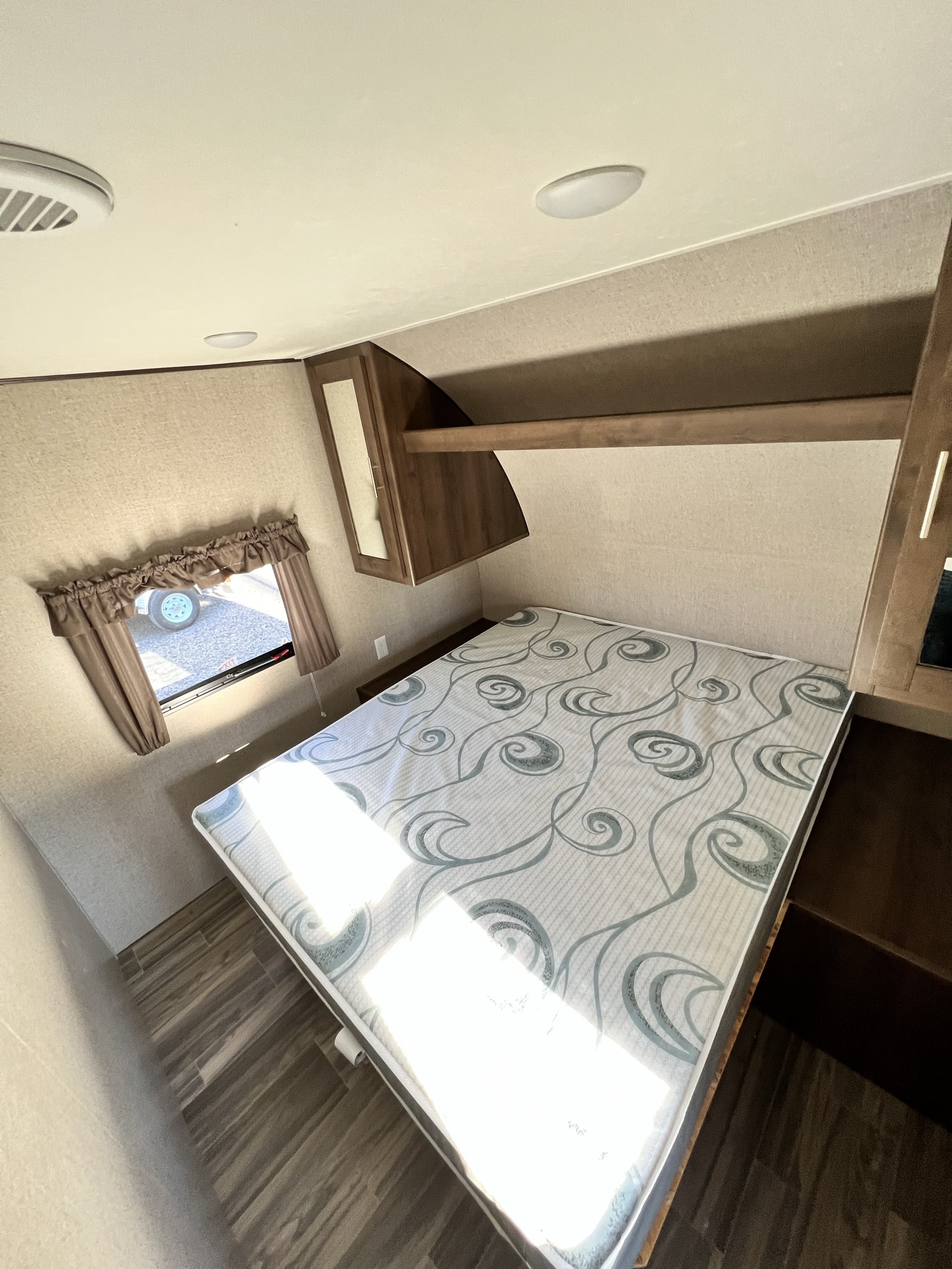 Cozy RV rental bedroom with patterned mattress, overhead storage, and a window view. Perfect for your next adventure.. Shasta 26BH 2020