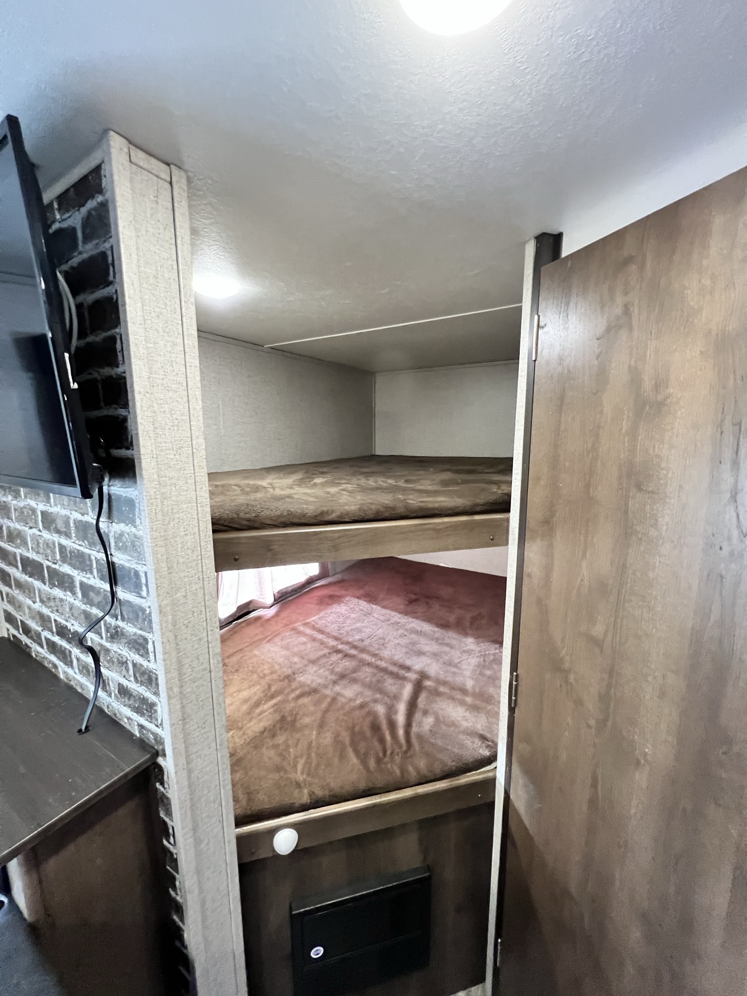 RV rental's cozy bunk beds with brown blankets, plus a mounted TV on a brick-patterned wall.. Shasta 26BH 2020