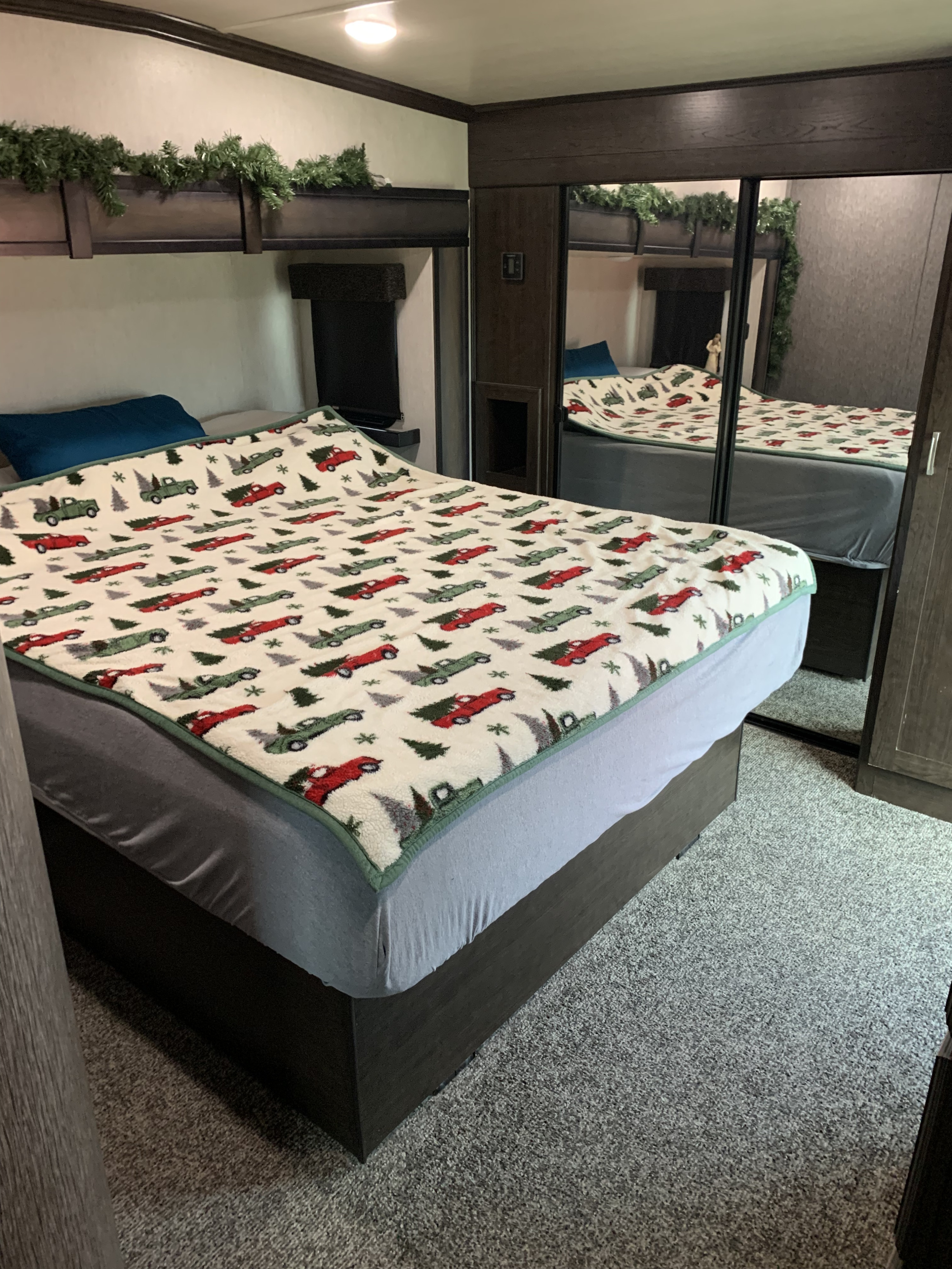 This RV rental bedroom features a bed with a festive car blanket, green garland decor, and a mirrored closet.. Heartland RVs Elkridge 2019