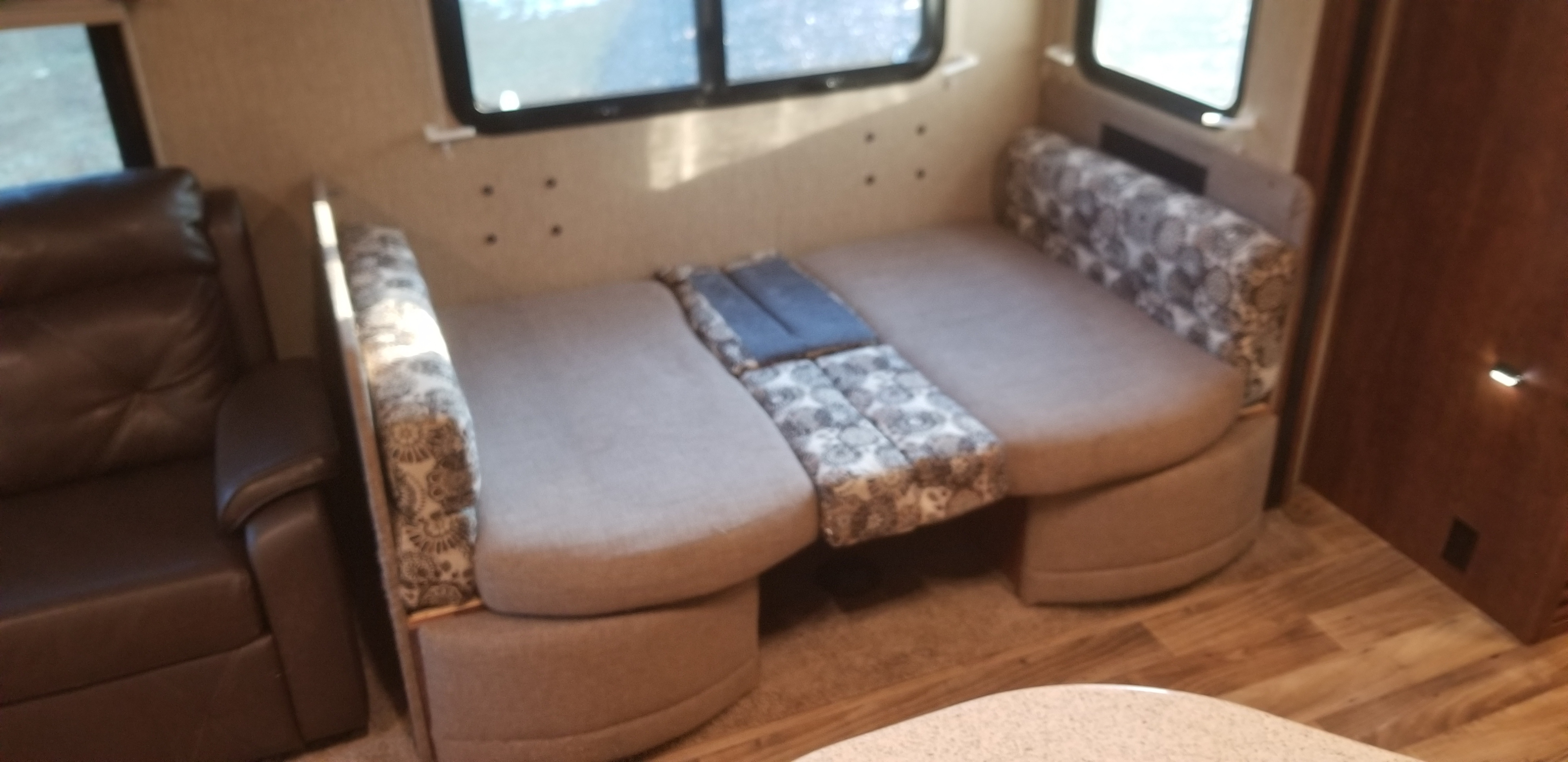 RV rental interior shows dinette converted to a bed, with a brown recliner, providing flexible living space.. Keystone RV Outback Super-Lite 2017