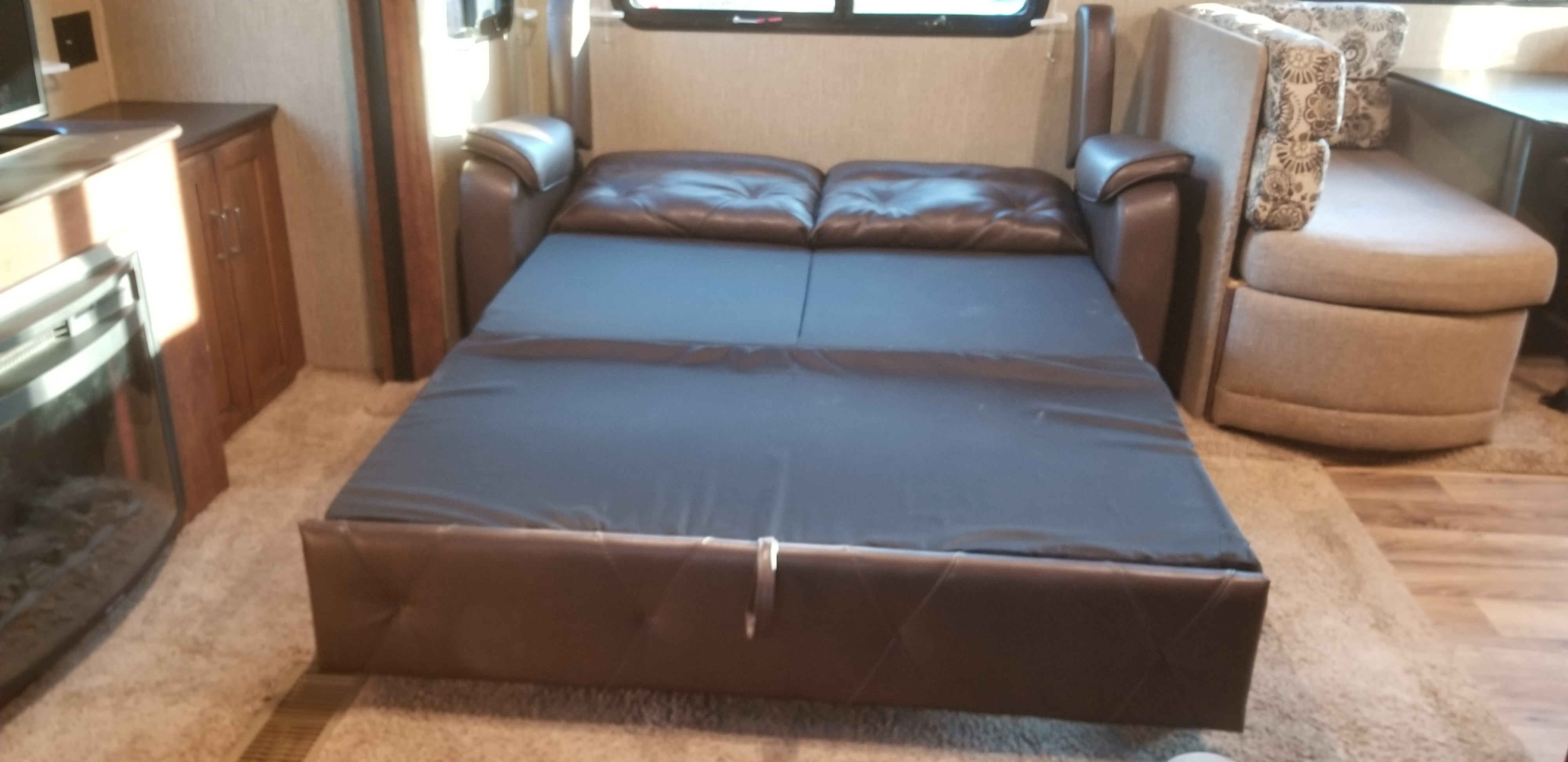 RV rental interior: Brown leather sleeper sofa extended as a bed, with entertainment unit and dinette.. Keystone RV Outback Super-Lite 2017
