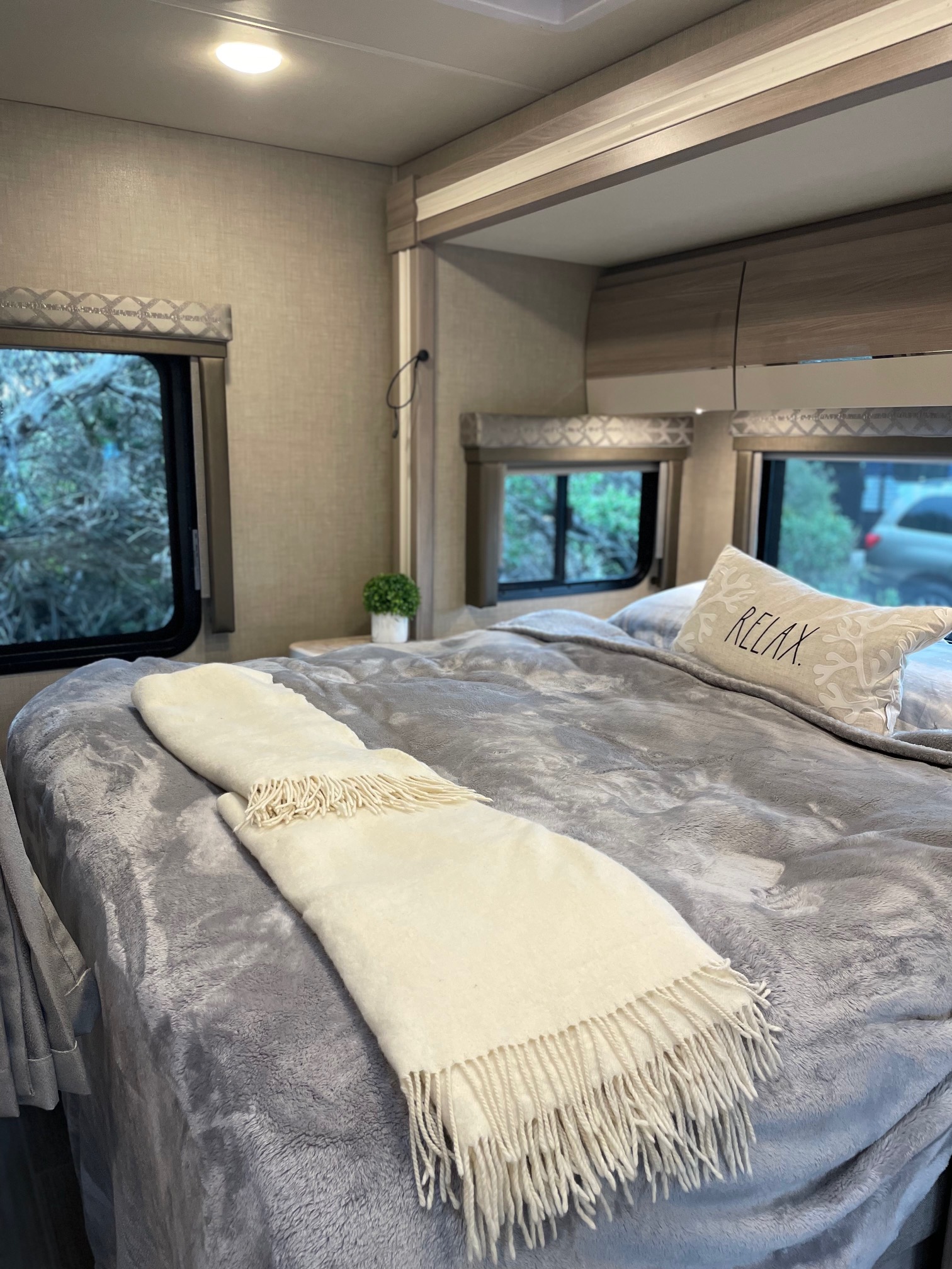 Inside a comfortable RV rental bedroom, featuring a large bed with a plush grey blanket and a "RELAX" pillow.. Mercedes Delano Sprinter 2022