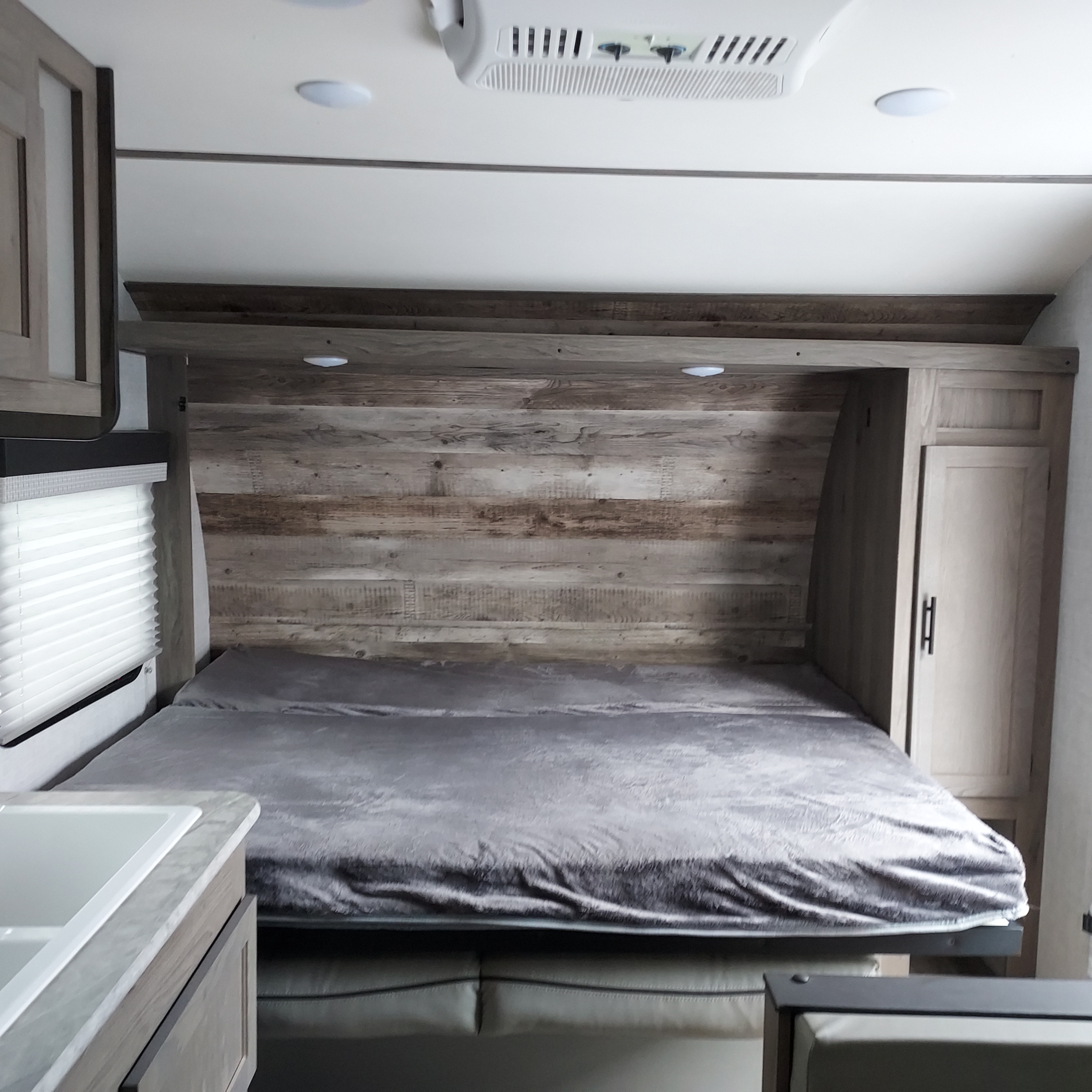 Comfortable RV rental bedroom with a bed, wood-paneled headboard, and practical overhead storage.. Amerilite 197BH 2021