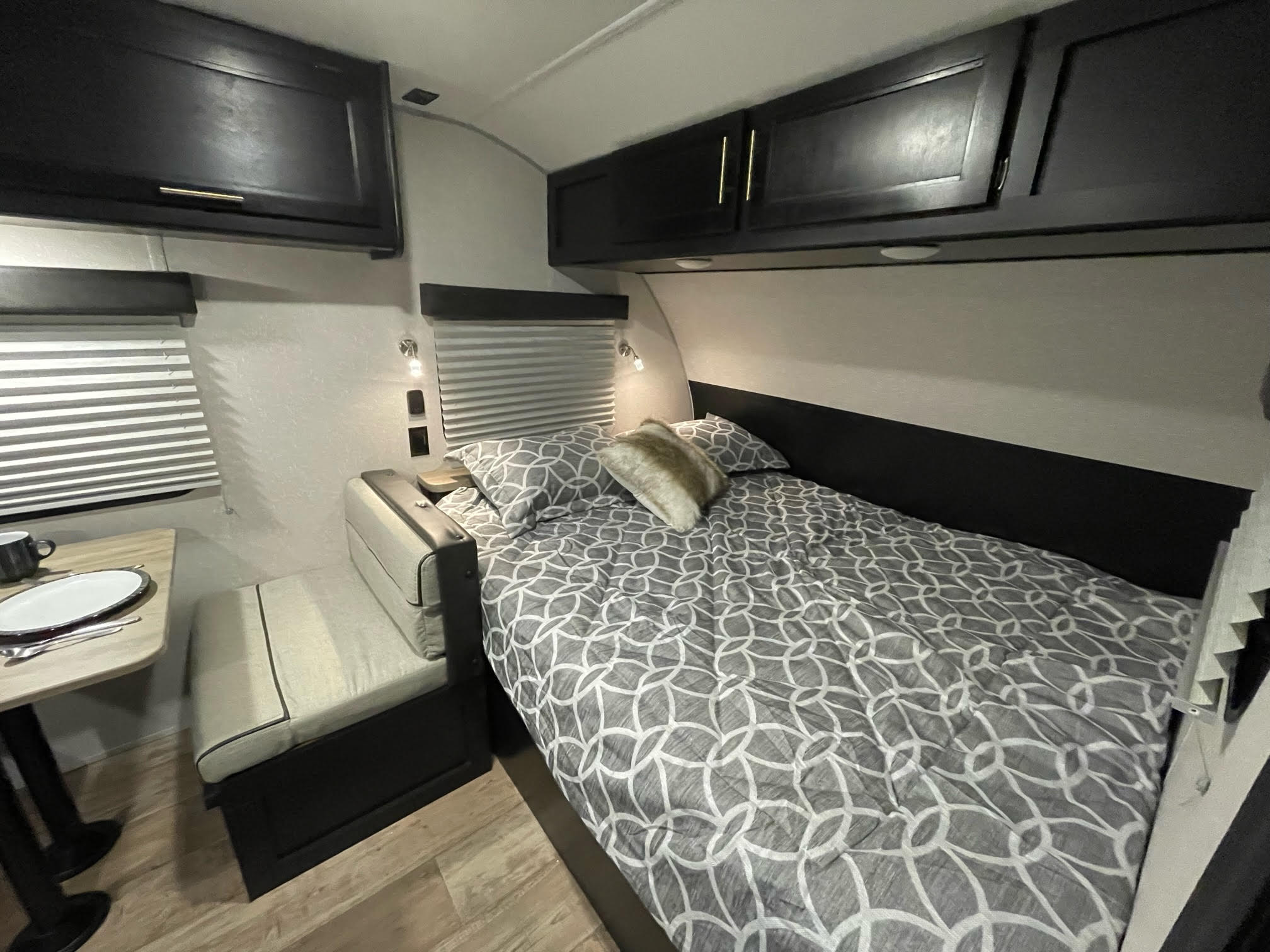 Compact and functional RV rental interior featuring a bed with patterned bedding, a small dining table, and overhead storage.. Forest River Cherokee Wolf Pup Black Label 2022