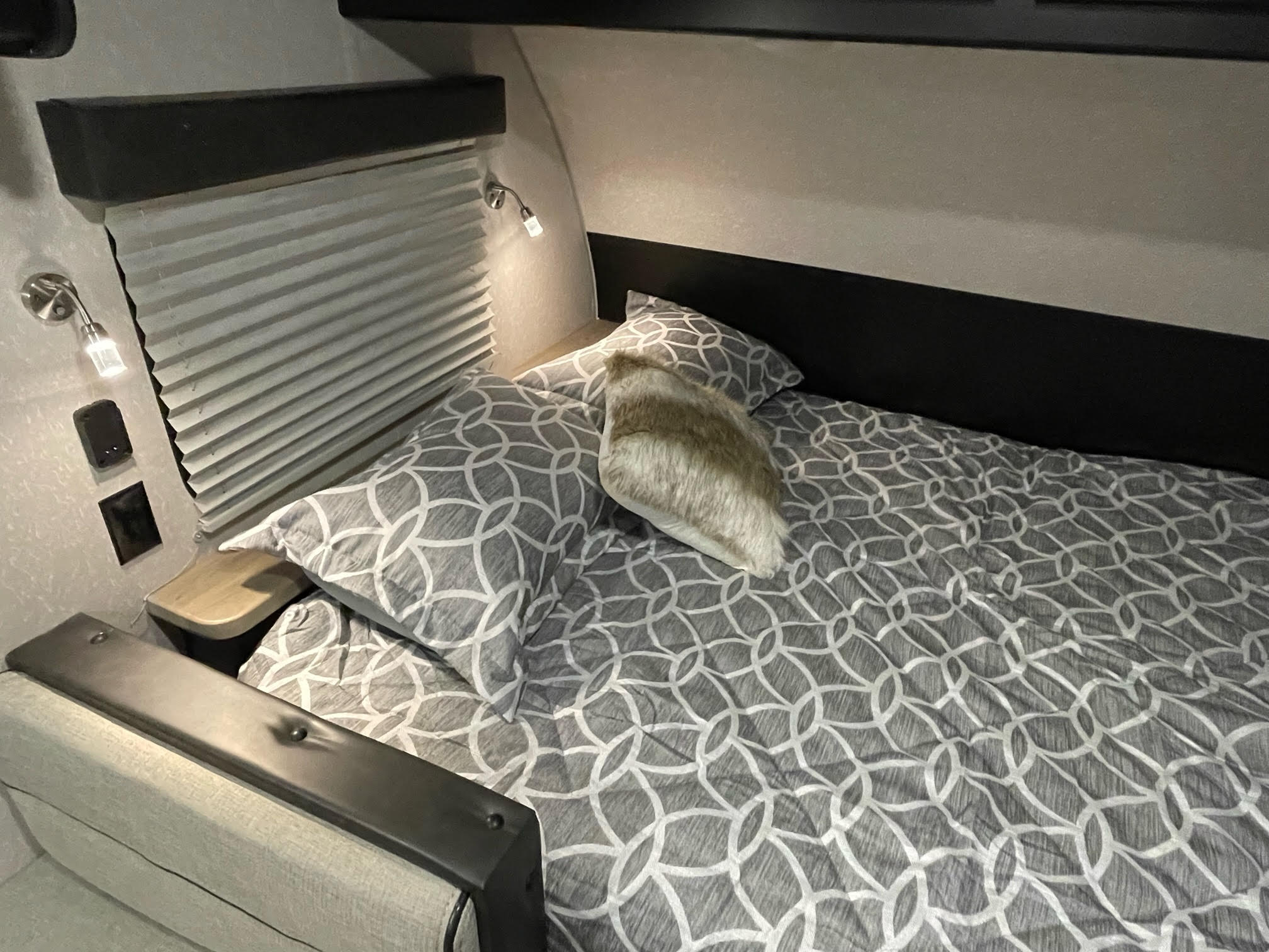 Cozy RV rental bedroom with patterned bedding, a reading light, and compact design elements for comfort.. Forest River Cherokee Wolf Pup Black Label 2022