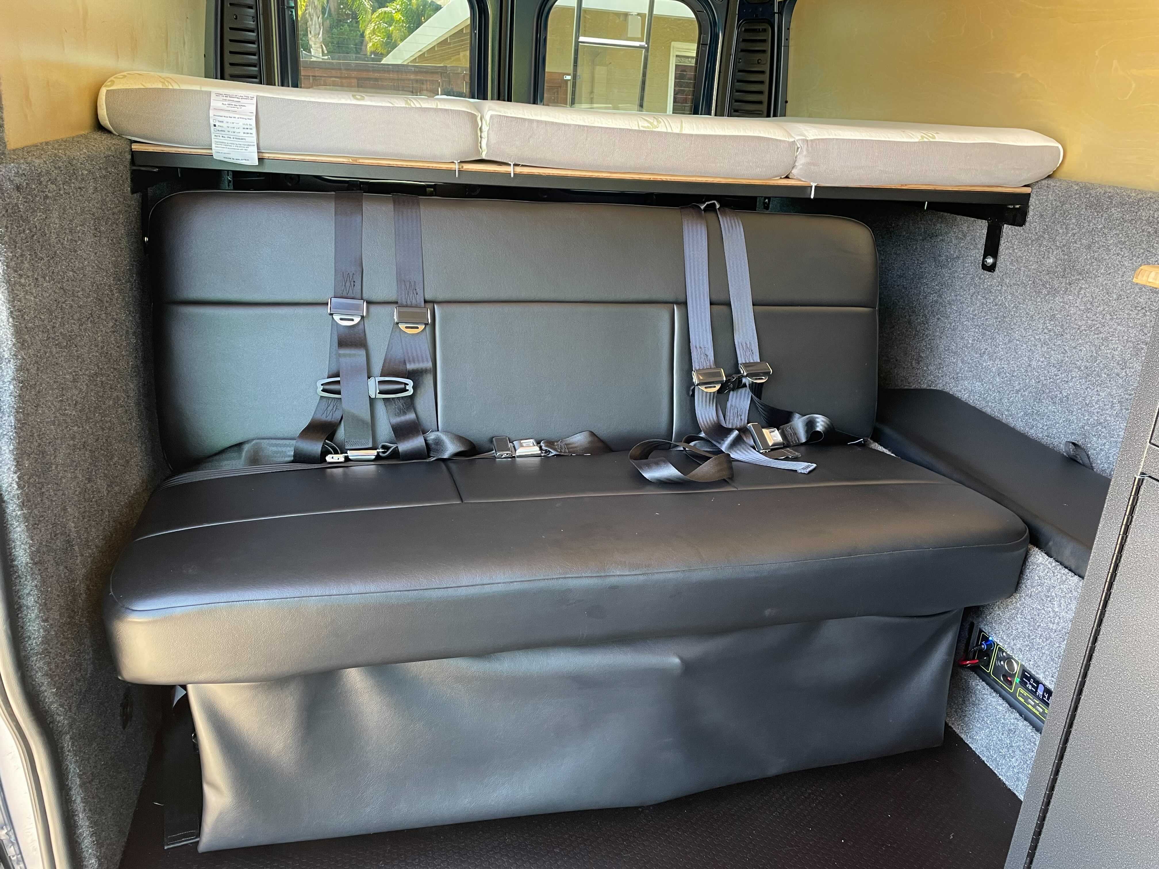 RV rental interior: black bench seat with seatbelts, upper bunk bed, and integrated control panel for comfortable travel.. Dodge Ram Promaster 250020 2021