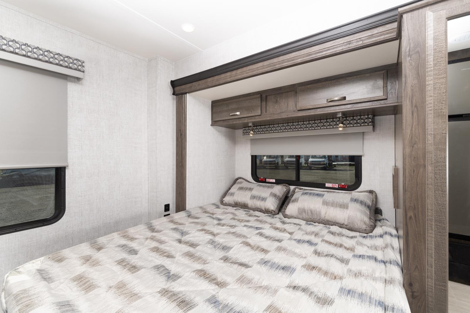Comfortable RV rental bedroom features a patterned bed, pillows, overhead storage, and a window. Perfect for a relaxing travel experience.. Gulf Stream Conquest 2022