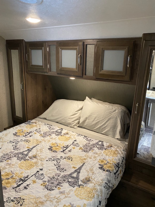 This RV rental's compact bedroom features a bed, overhead cabinets, and mirrored closets for a comfortable stay.. Keystone Passport 2019
