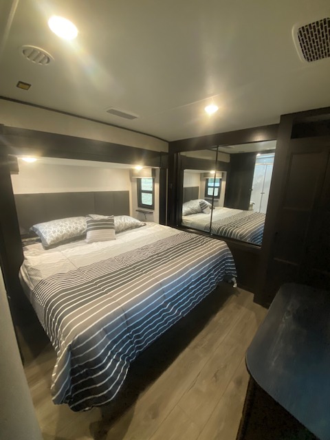Spacious RV rental bedroom featuring a striped bed, mirrored closet, wood flooring, and bright ceiling lights.. Open Range Open Range 2021