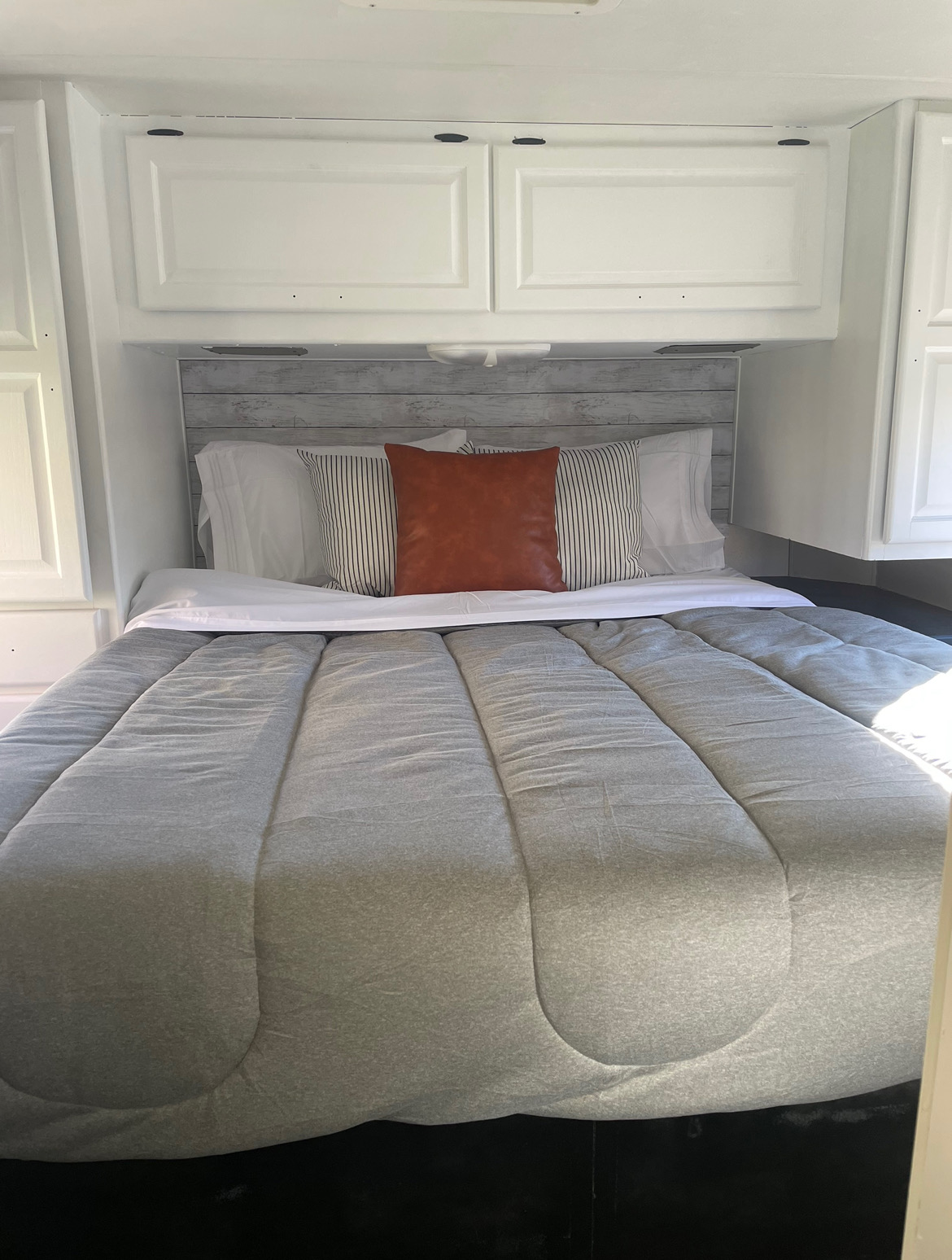 Cozy RV rental bedroom featuring a comfy bed with gray comforter, striped and rust pillows, and white overhead cabinets.. Four Winds Majestic 2010