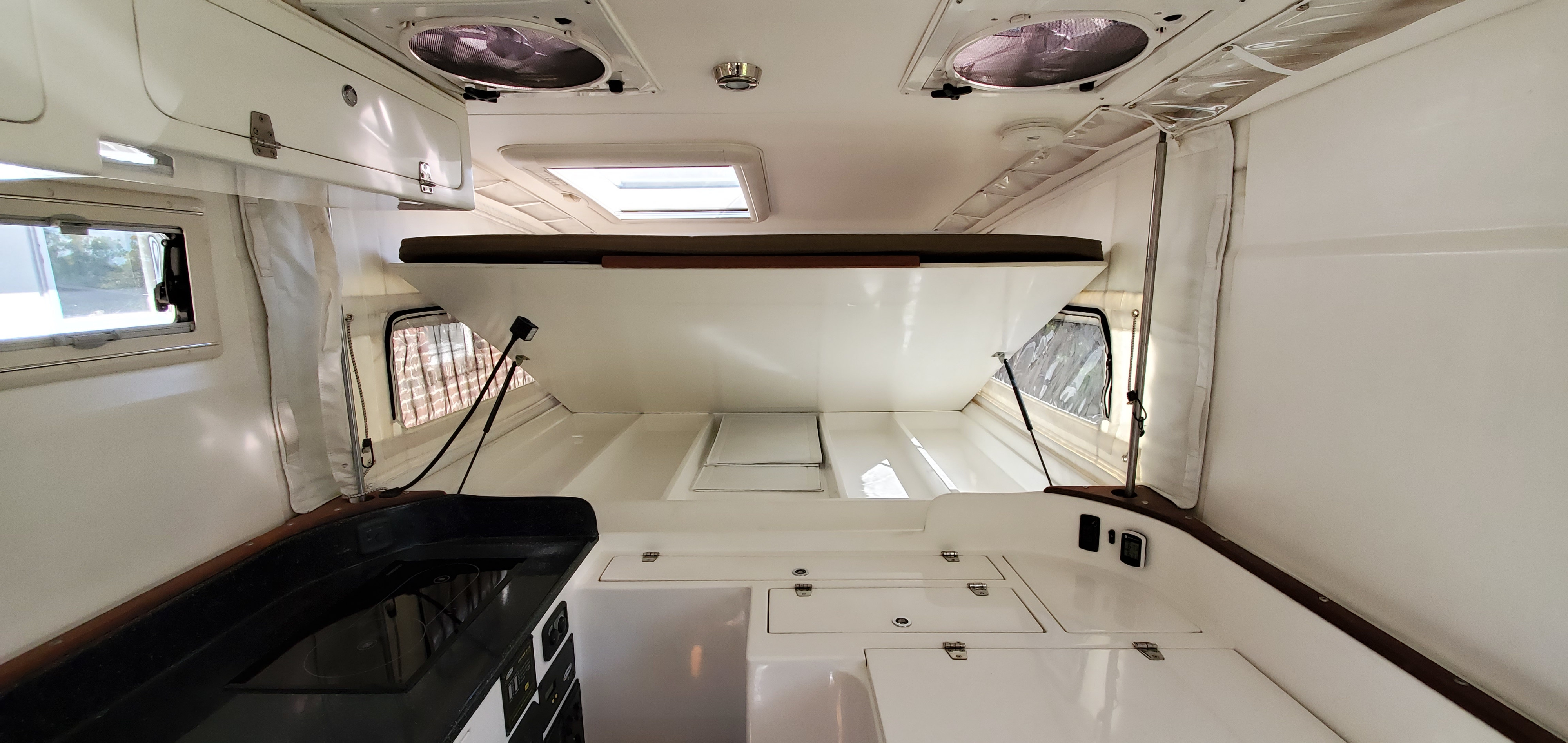 Clean RV rental interior showing a raised bed, compact galley, and white storage compartments.. xp Camper 2012