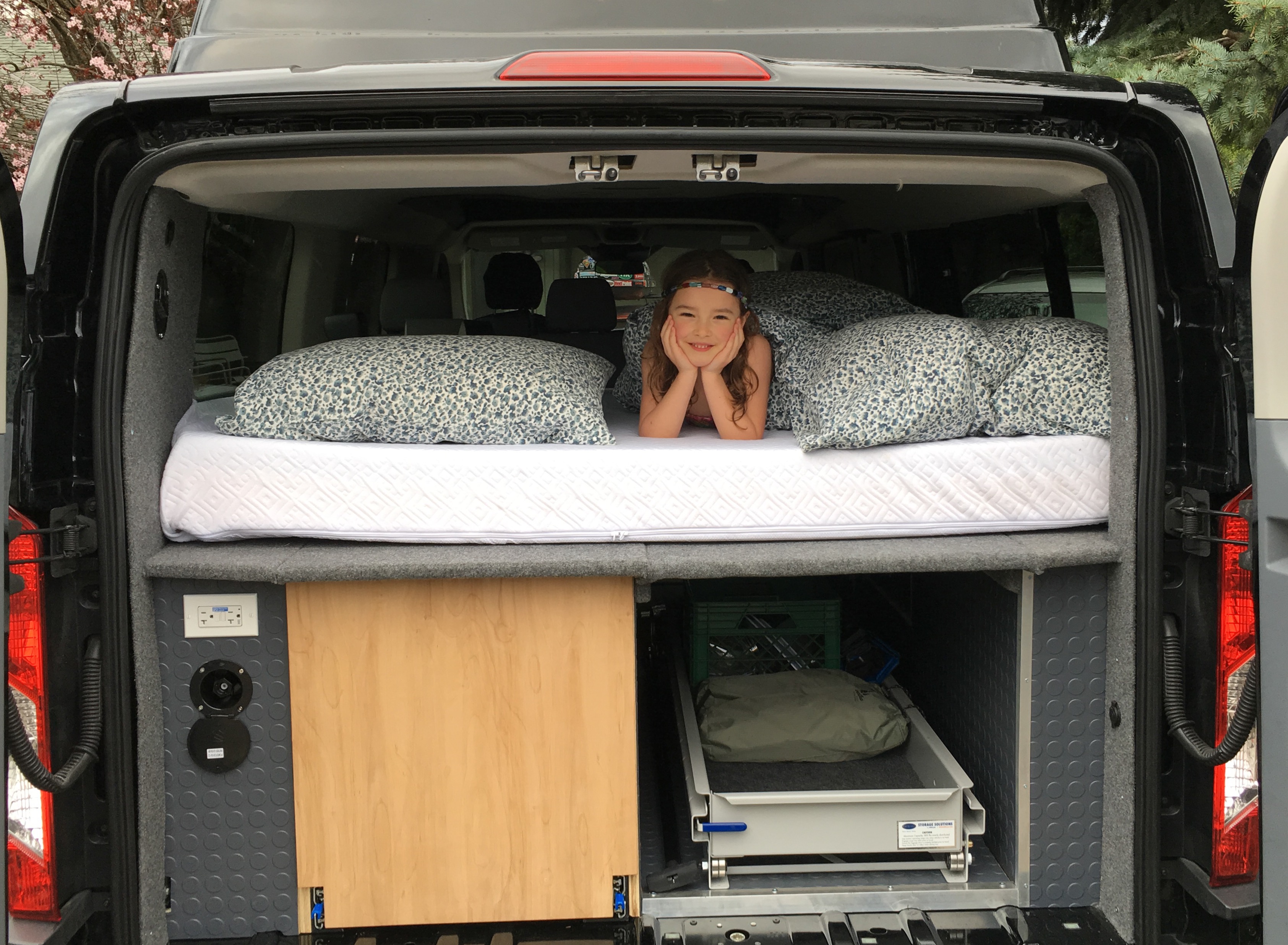Experience comfort on the road: a custom bed and smart storage in this RV rental van, featuring a smiling girl.. Ford Van 2018