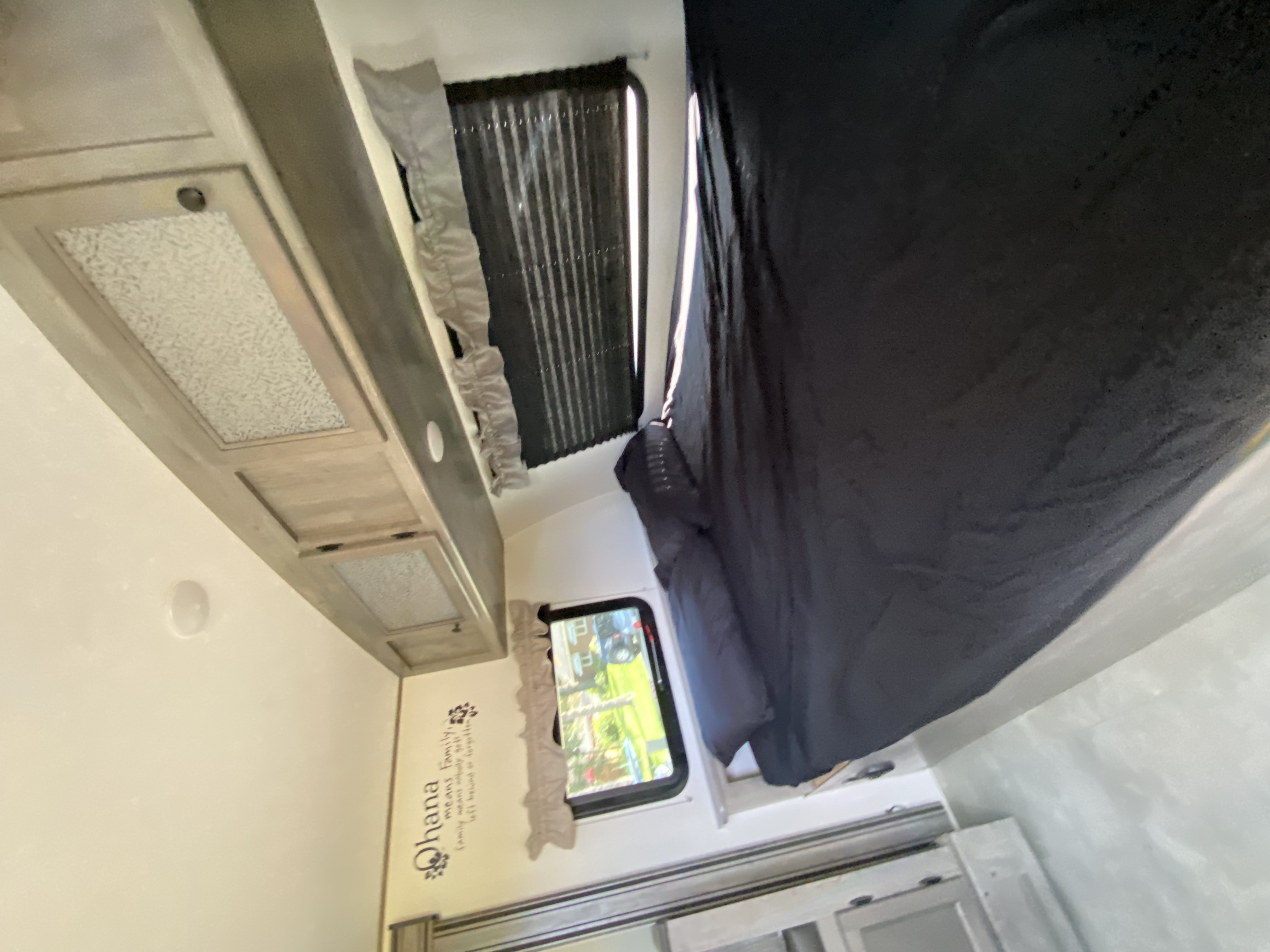 Explore this cozy RV rental bedroom: dark bedding, light wood cabinets, and a window with scenic views. Features an "Ohana" wall decal.. Coachmen Apex Nano 194 BHS 2021