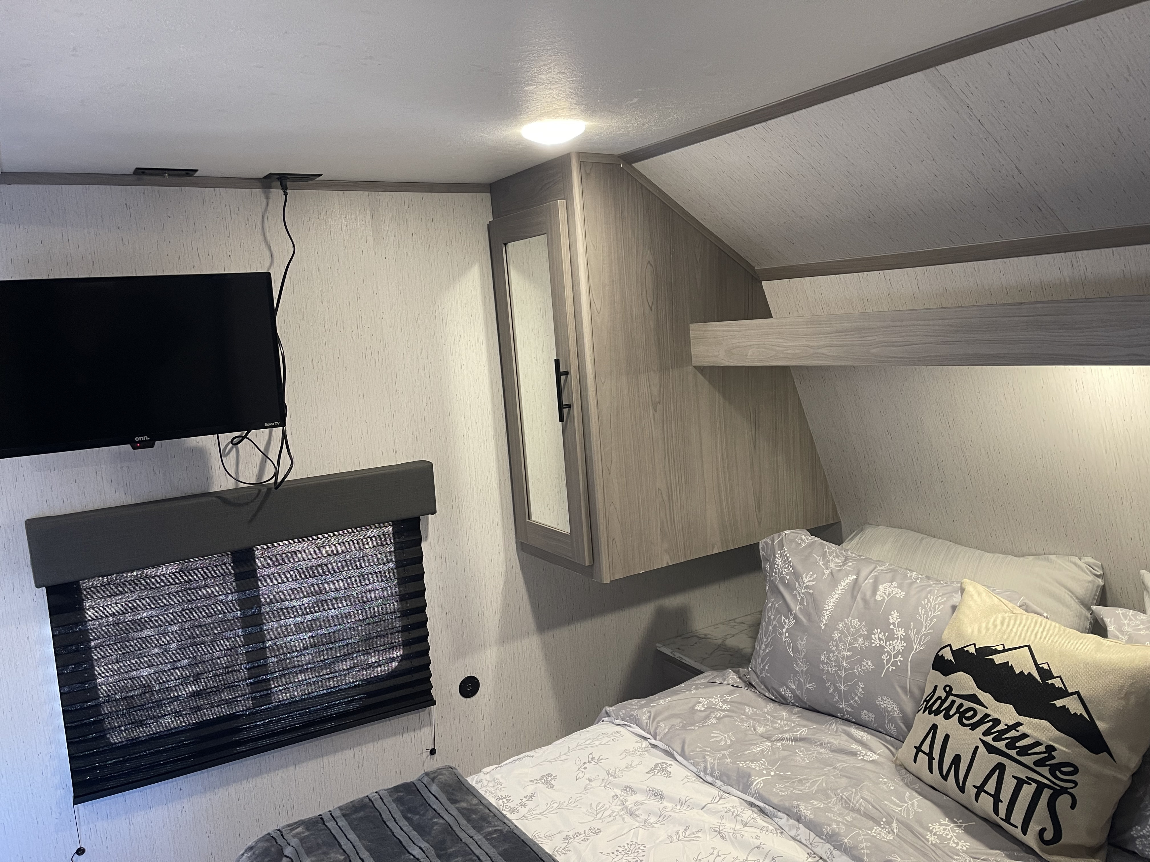 Cozy RV rental bedroom with TV, window, storage, and an "Adventure Awaits" pillow for comfortable travels.. Dutchmen Coleman 2022