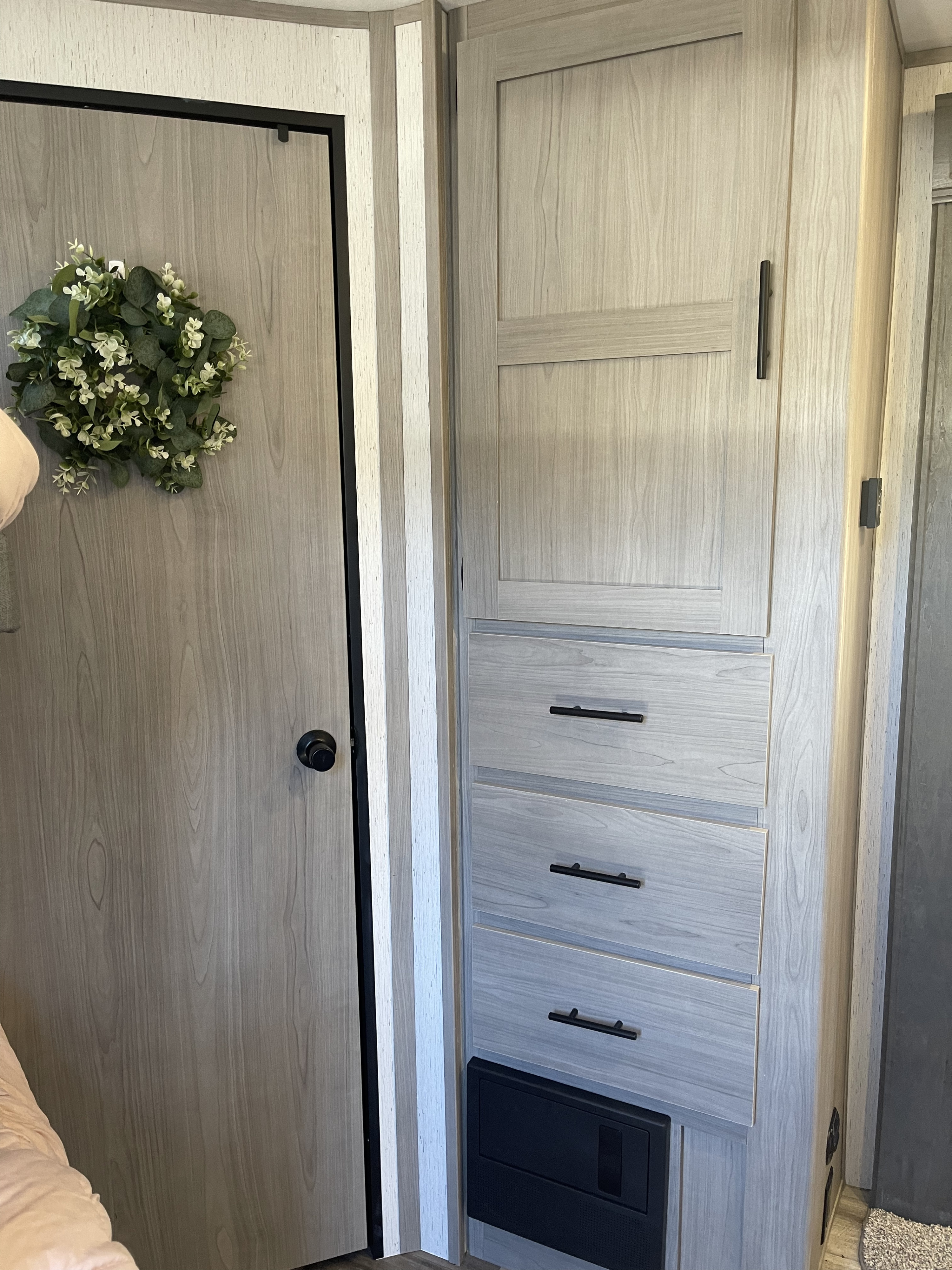 Modern RV rental interior: Light wood door with wreath, storage cabinets, and drawers with black hardware.. Dutchmen Coleman 2022