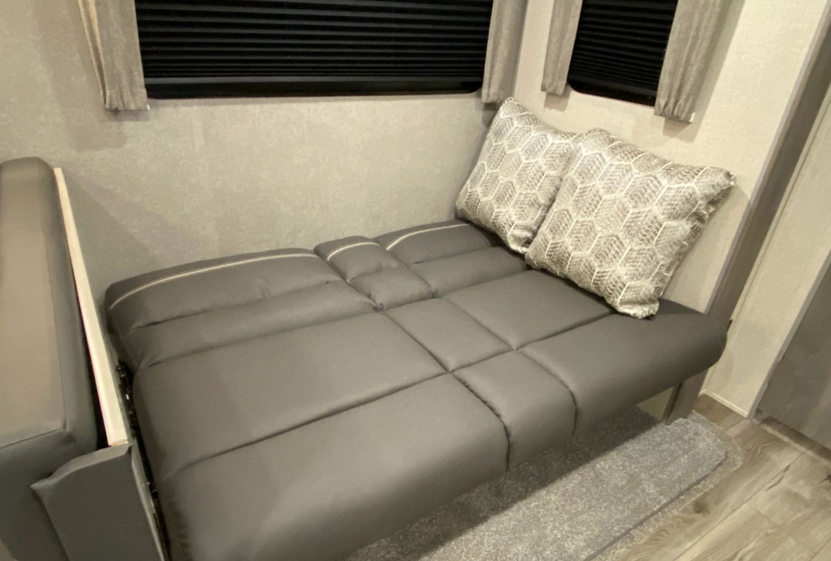 Gray segmented sofa unfolded as a bed, with two patterned pillows, inside an RV rental. Ideal for travel comfort.. Coachmen Catalina 2022