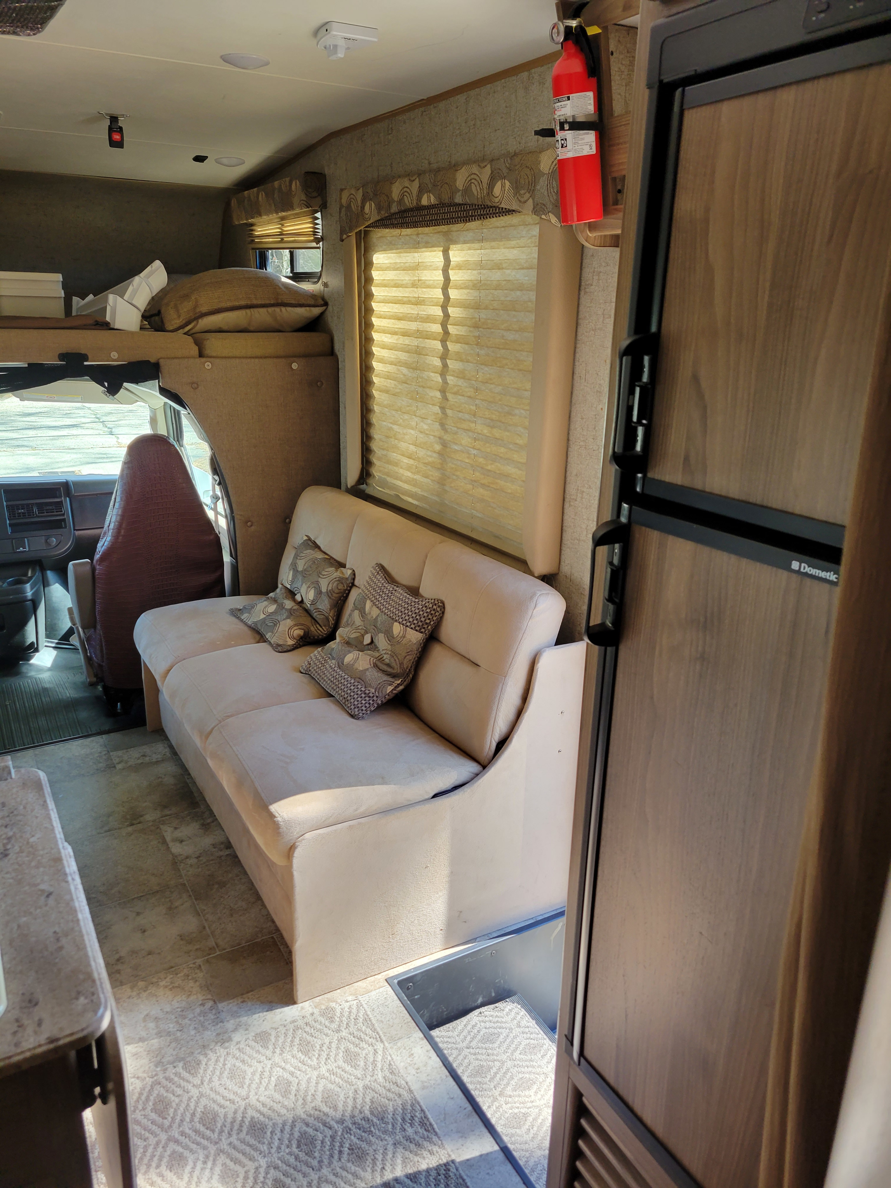 Explore this rv rental's interior: comfy sofa with pillows, large window, Dometic fridge, and spacious driver's cab area.. Coachmen Freelander 2017