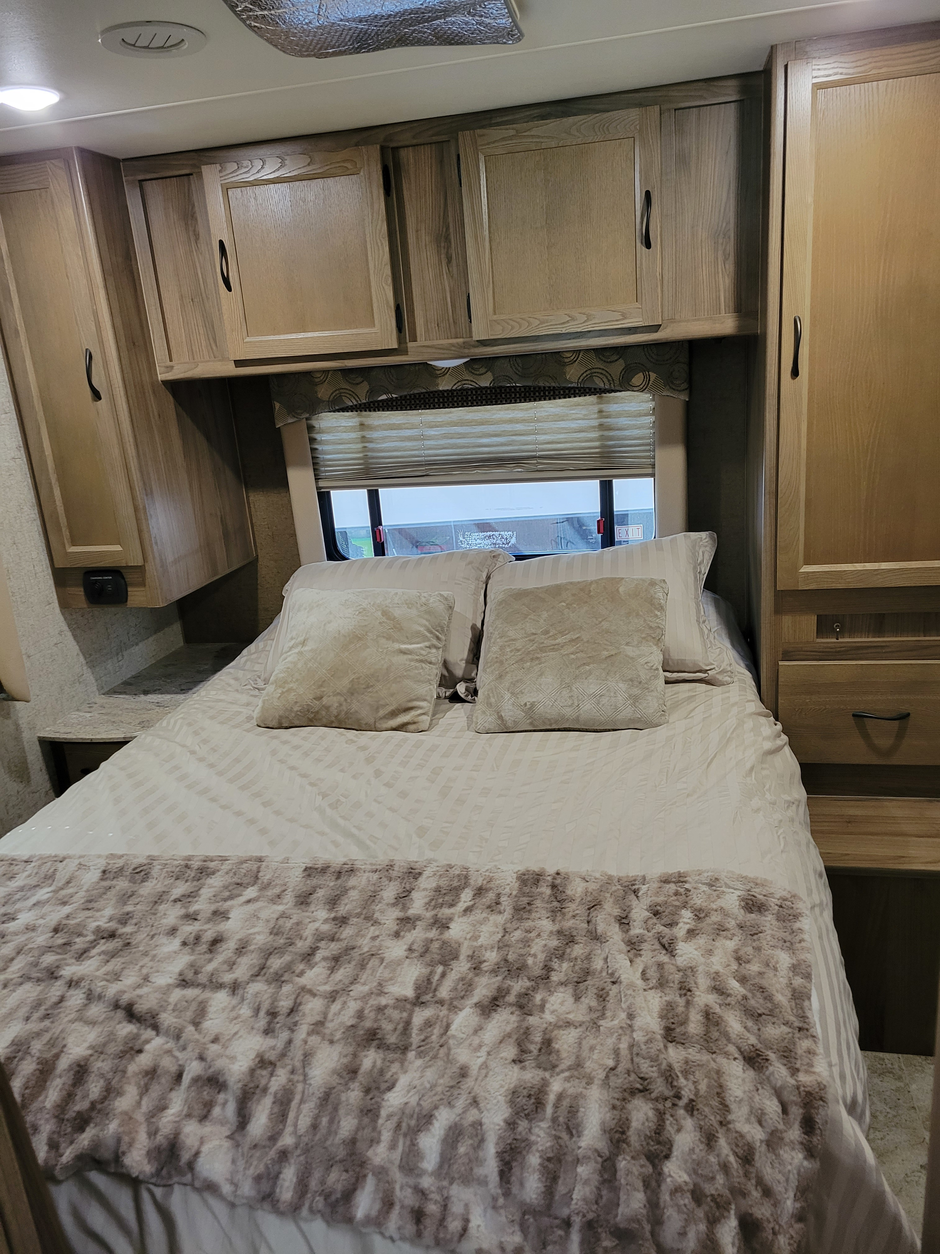 Cozy RV rental bedroom featuring wood cabinets, a comfy bed with a fluffy blanket, and a window with blinds.. Coachmen Freelander 2017