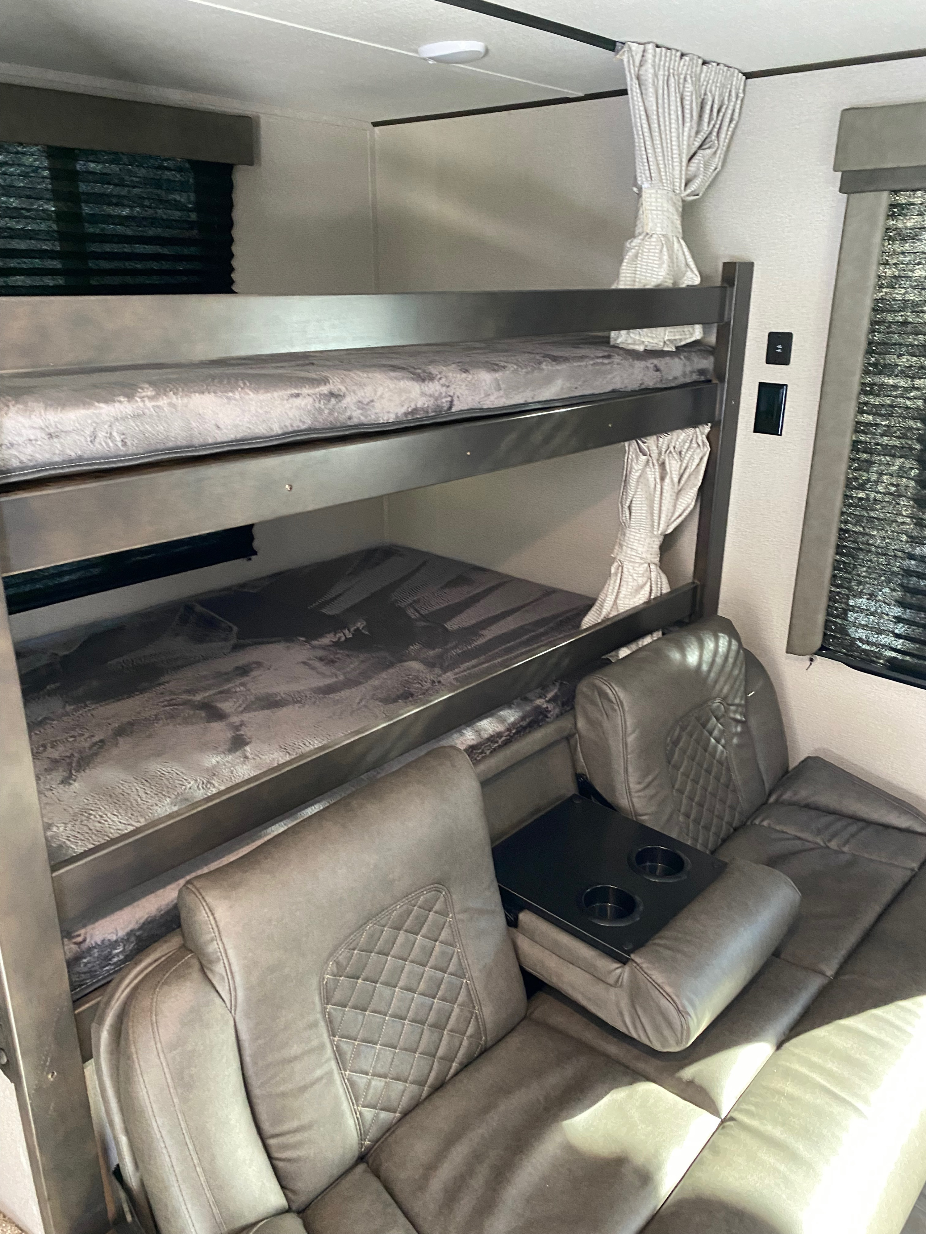 Cozy RV rental interior featuring comfortable bunk beds with soft mattresses, a plush recliner sofa with cup holders, and privacy blinds.. Grand Design Transcend Xplor 265BH 2022